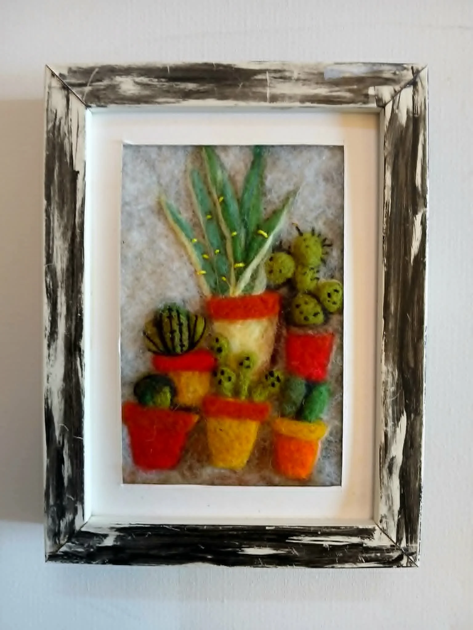 A framed artwork of a colorful still life with fruit and potted plants, displayed on a wall.