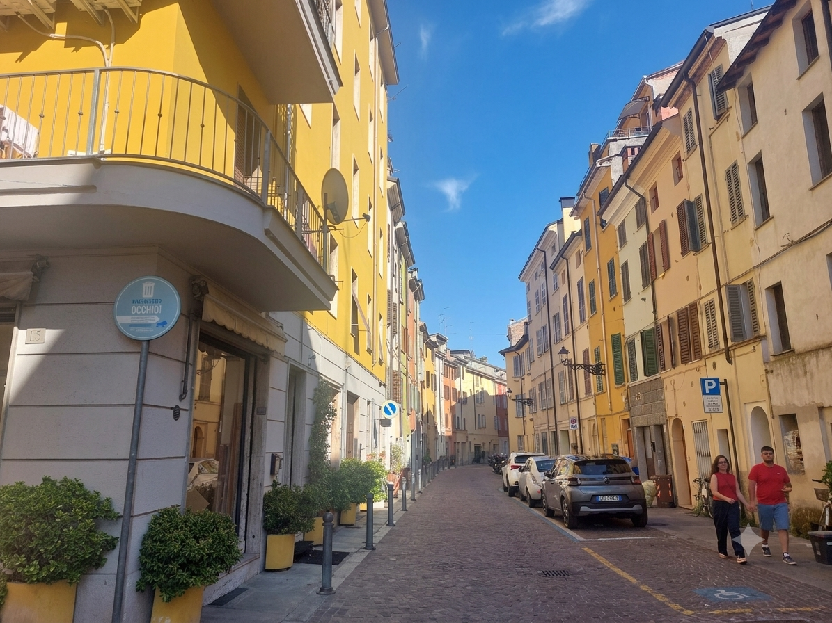 Strada pedonale in un quartiere residenziale con edifici di colore giallo e beige, parcheggio con auto, persone che camminano e cartelli stradali