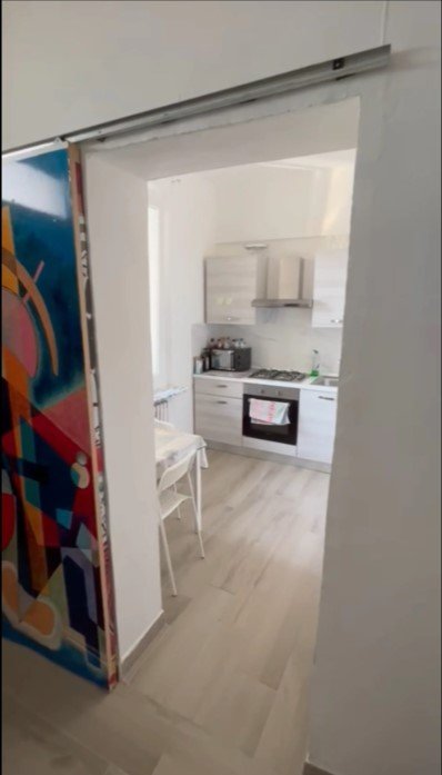 Vista di una cucina moderna con armadietti bianchi, fornello e forno, vista dal corridoio.
