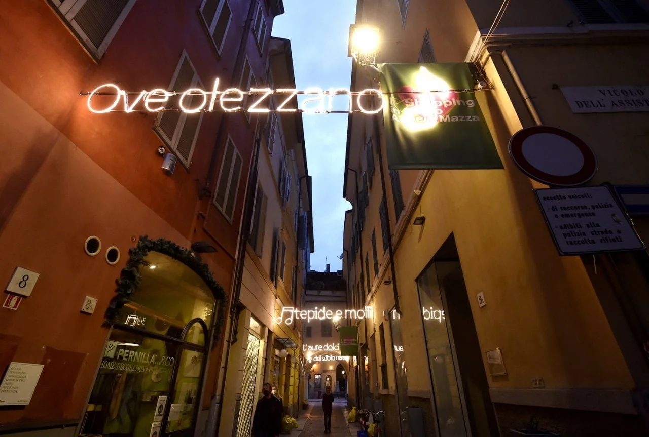 Strada stretta con edifici colorati, insegne di luci al neon e persone che camminano, cielo serale