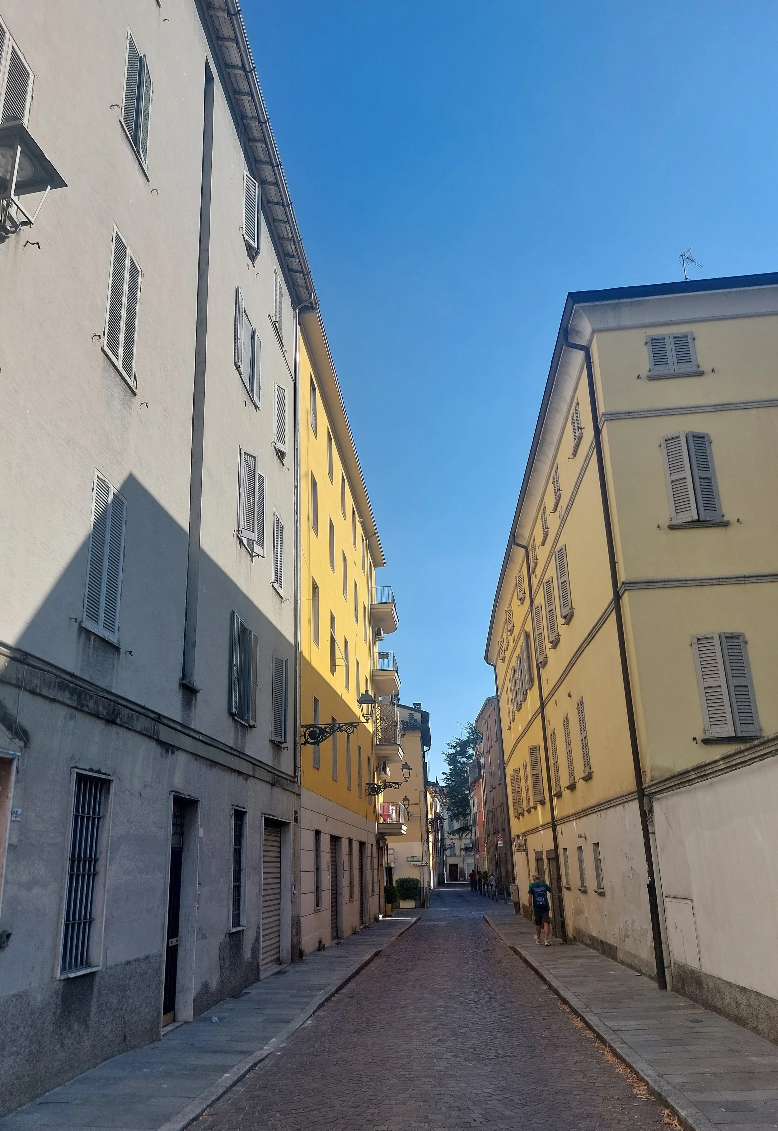 Una strada stretta tra edifici di colore giallo e grigio sotto un cielo azzurro