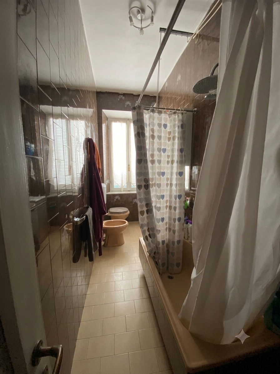 Bagno con vasca, tenda doccia a fiorellini, bidet e water, finestra e lampada sul soffitto.