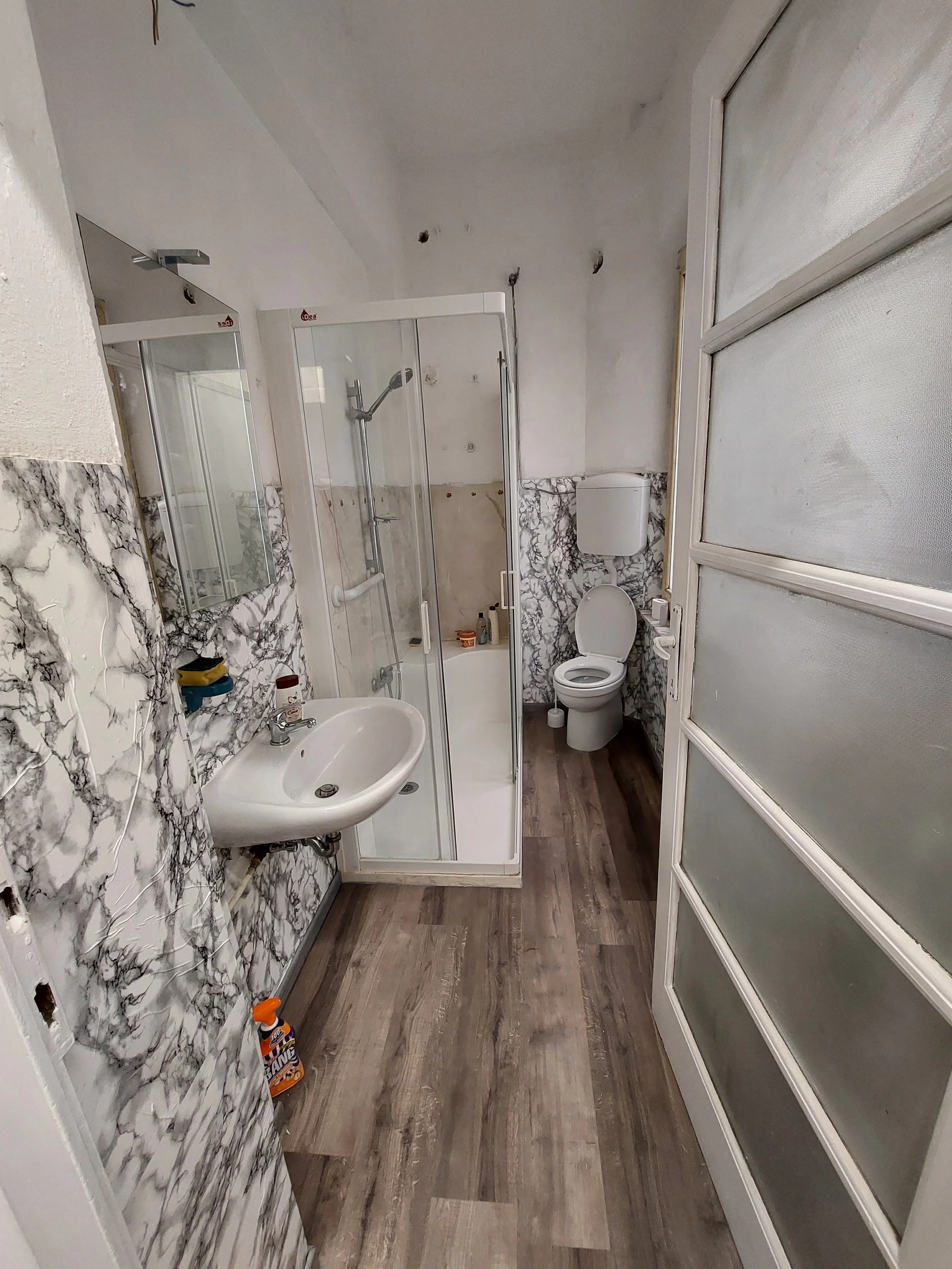Bagno in fase di ristrutturazione con pareti rivestite in marmo bianco e nero, sanitari nuovi e pavimento in legno.