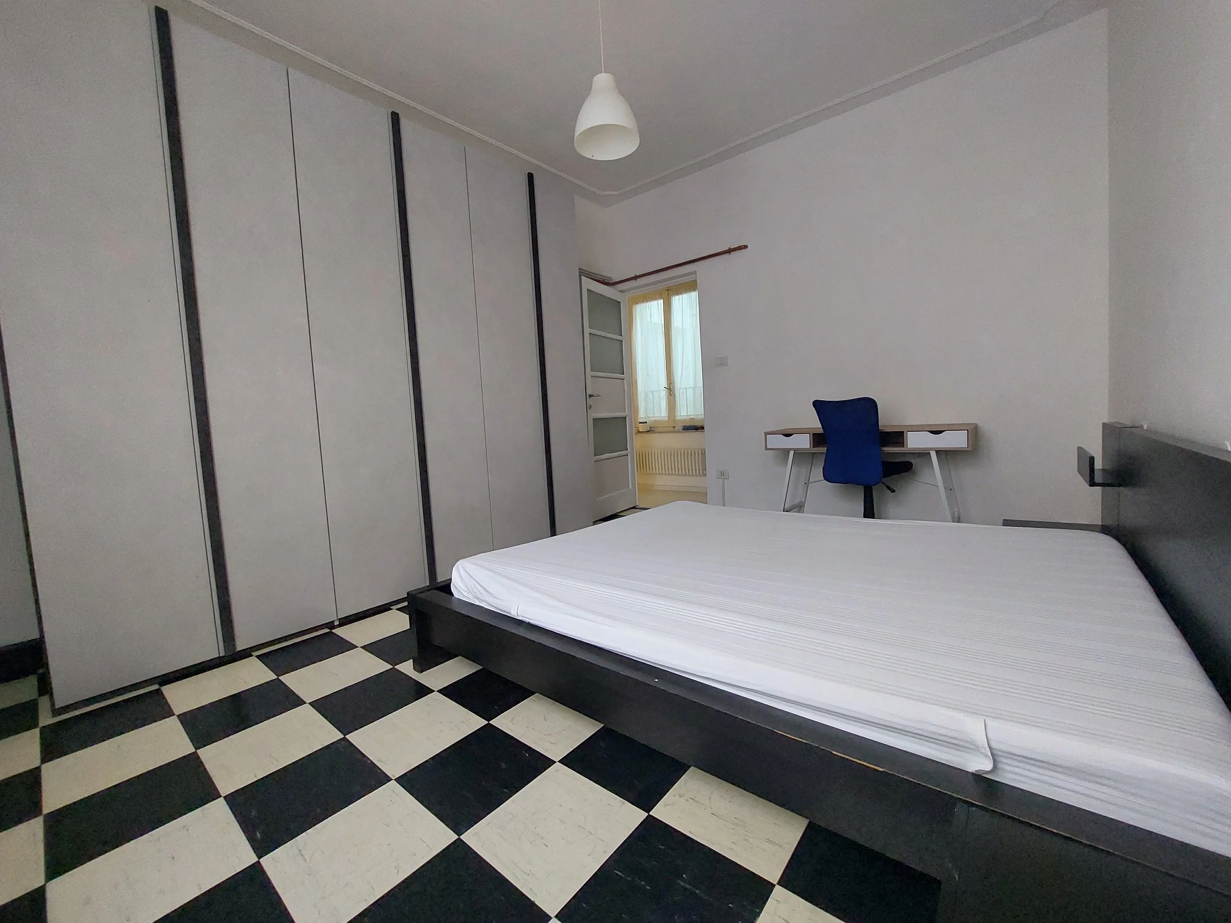 Camera da letto con letto matrimoniale, armadio a intercapedine bianco e nero, scrivania con sedia blu, finestra, illuminazione a soffitto.