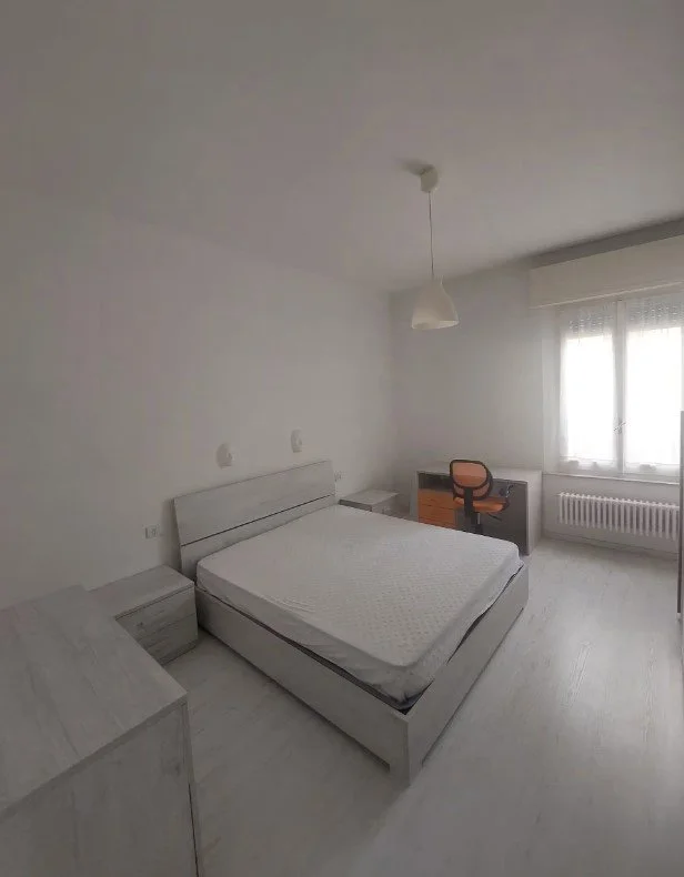 Stanza moderna e luminosa con letto matrimoniale, scrivania con sedia, armadio e finestra con tende
