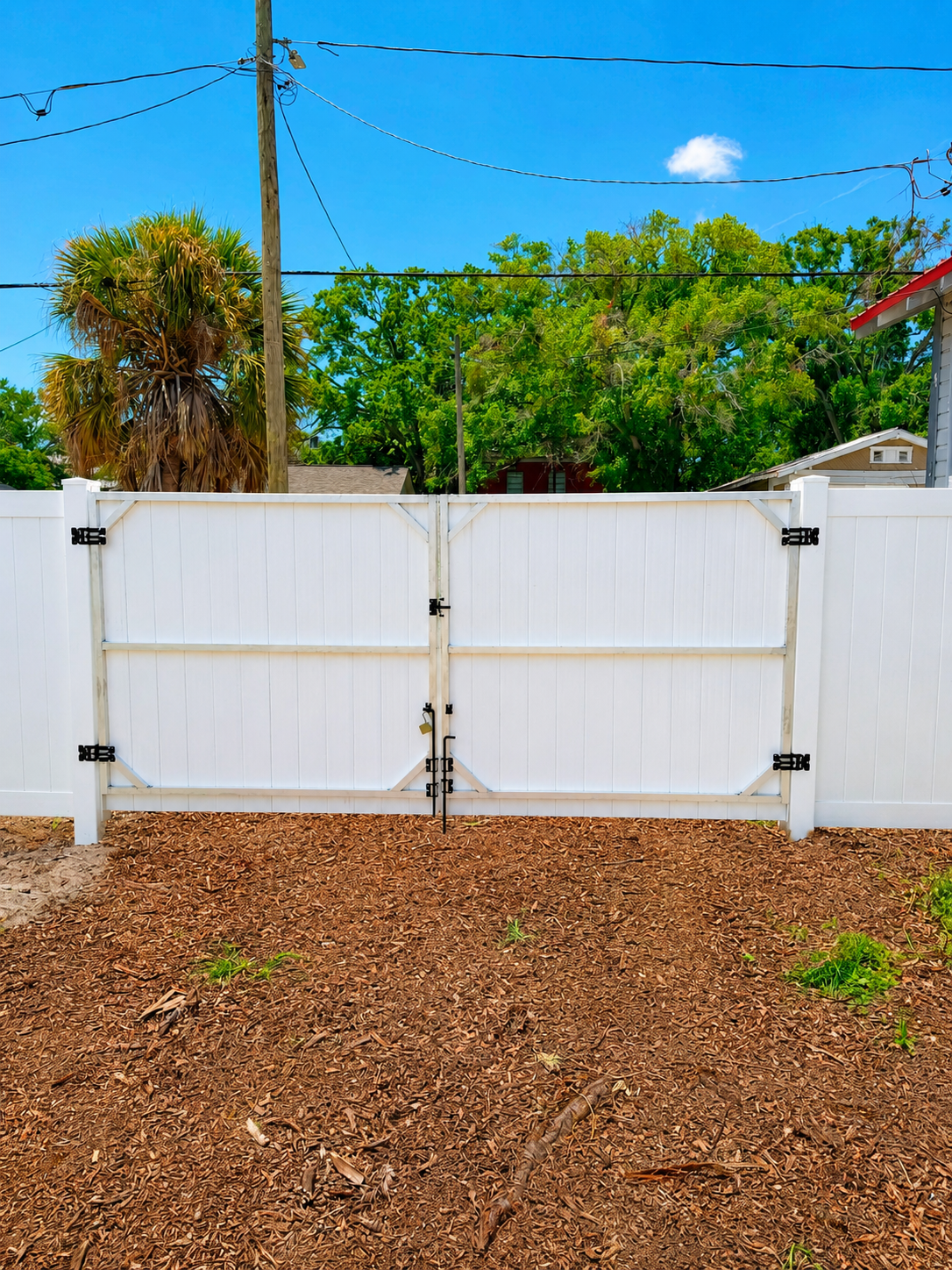White gate fence in a backyard with trees and a cloudy blue sky.