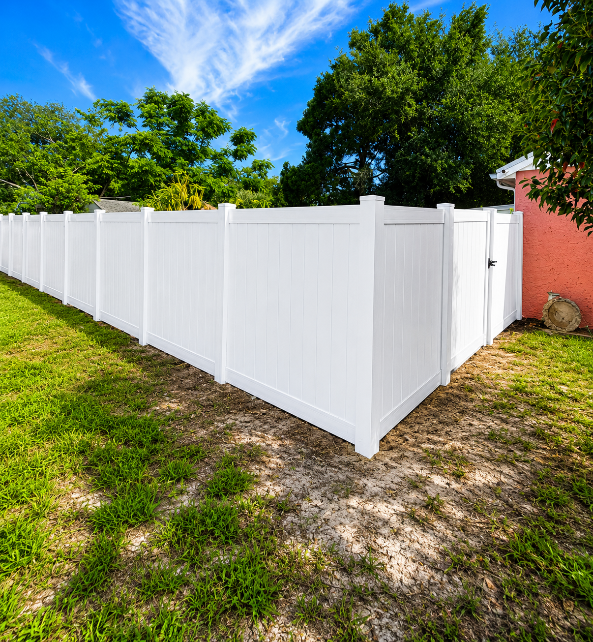 White vinyl privacy fence in a backyard with green grass, trees, blue sky, and a pink house wall.