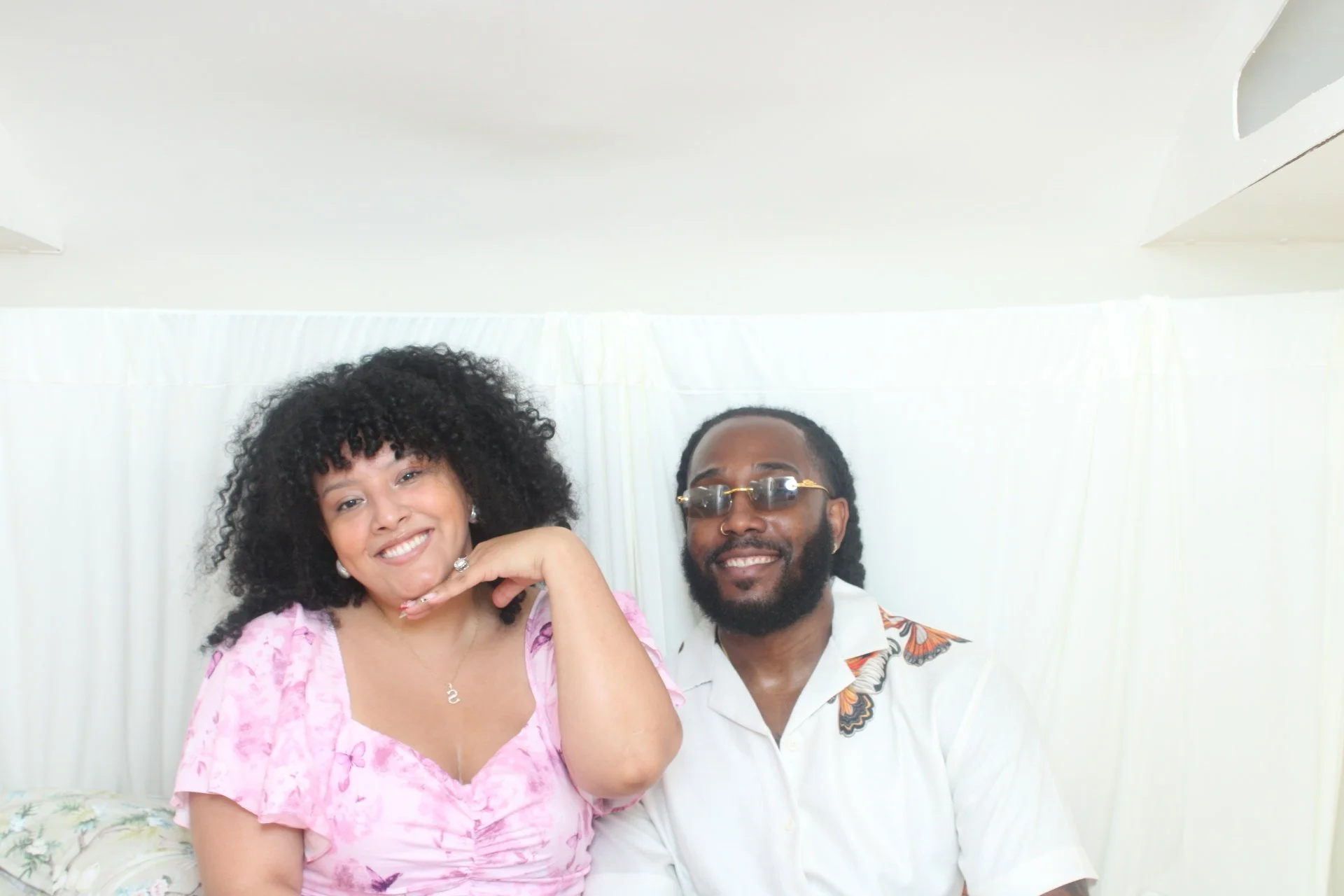 A woman with curly hair and a man with sunglasses and a beard, both smiling and posing together indoors.