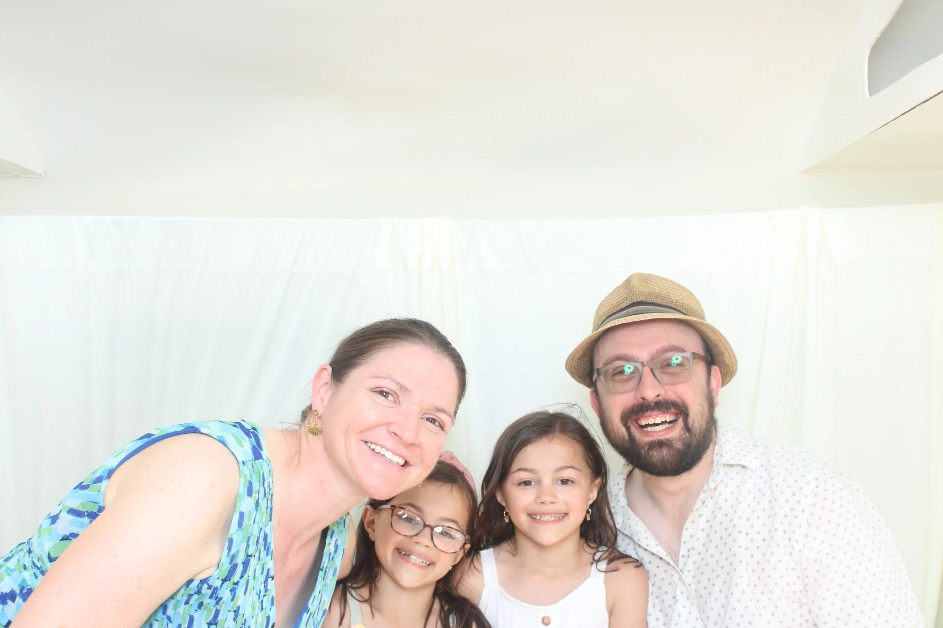 Family portrait of six people, including three adults and three children, smiling and close together against a white background.