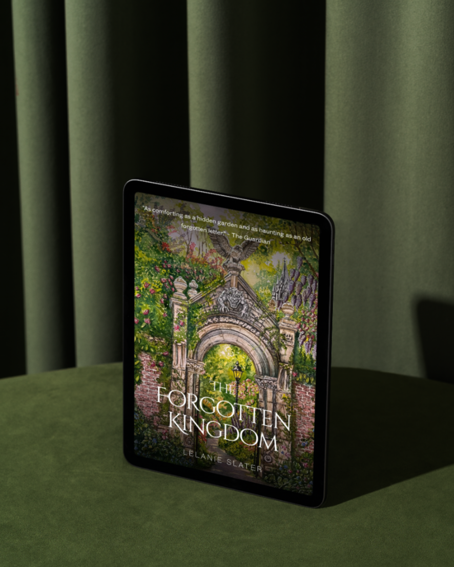 Cover of the book titled "The Forgotten Kingdom" by Liane Slater, displaying an illustration of an old stone archway surrounded by lush greenery and flowers, with a lamp post and castle towers in the background.