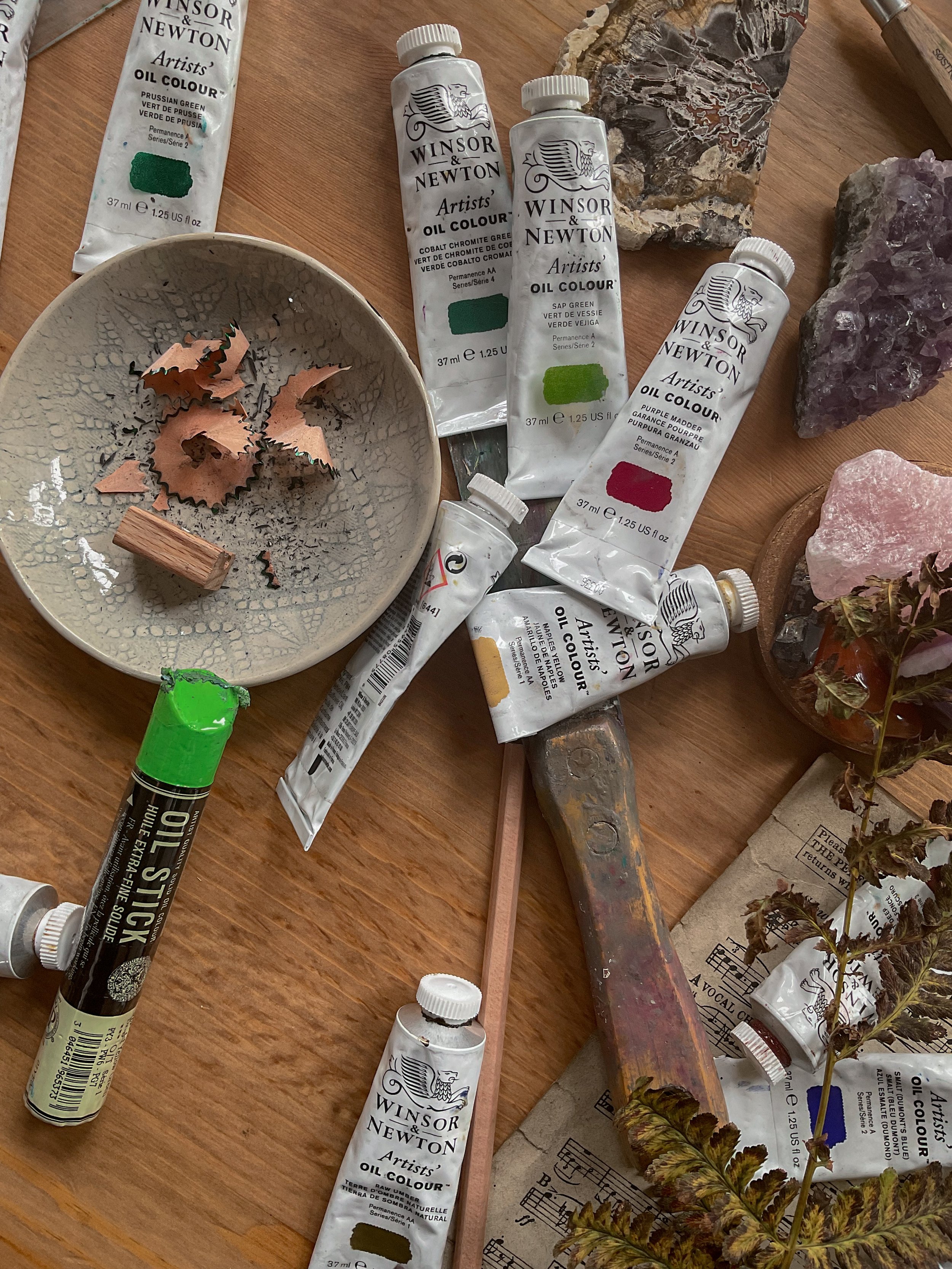 Professional Winsor & Newton oil paints, artist brushes and natural materials arranged on a wooden studio table for creative painting.