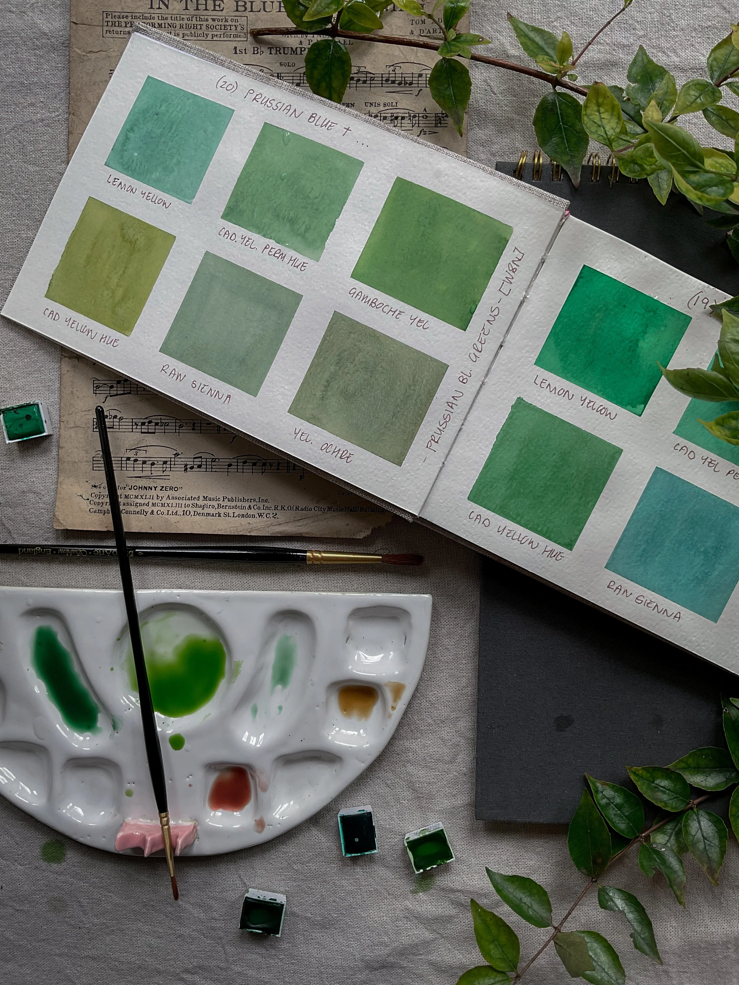 Watercolour colour mixing chart showing a range of botanical greens created using different blue and yellow pigments, alongside an artist's palette and brushes.
