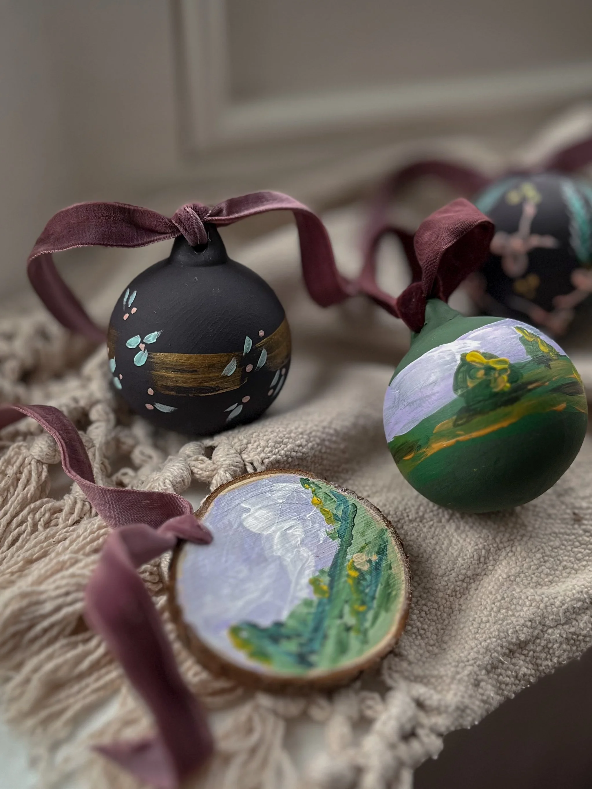 Collection of hand-painted ceramic Christmas baubles featuring original botanical, landscape and nature-inspired miniature artworks with burgundy ribbons.