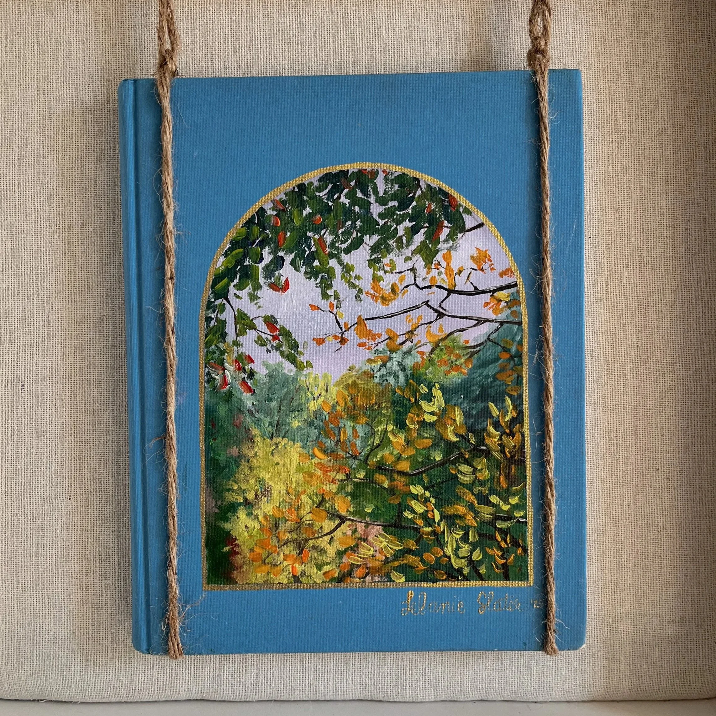 Close-up of a blue book cover with a circular, colorful abstract design. The book has rope details on its sides, and a small part of text at the bottom says 'Lorne Gofie'.