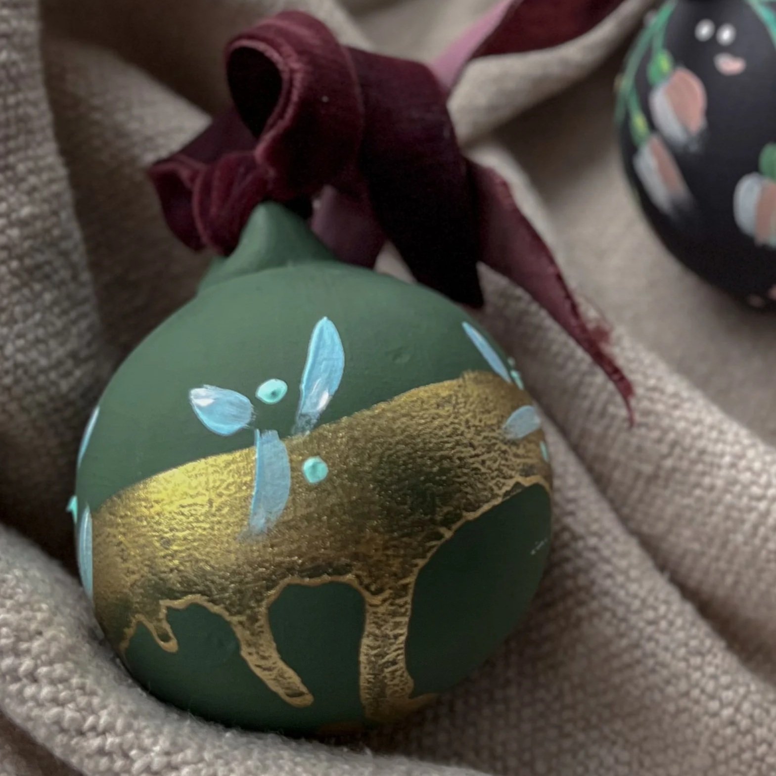 Hand-painted ceramic Christmas bauble featuring a blue flower, botanical details and gold accents.