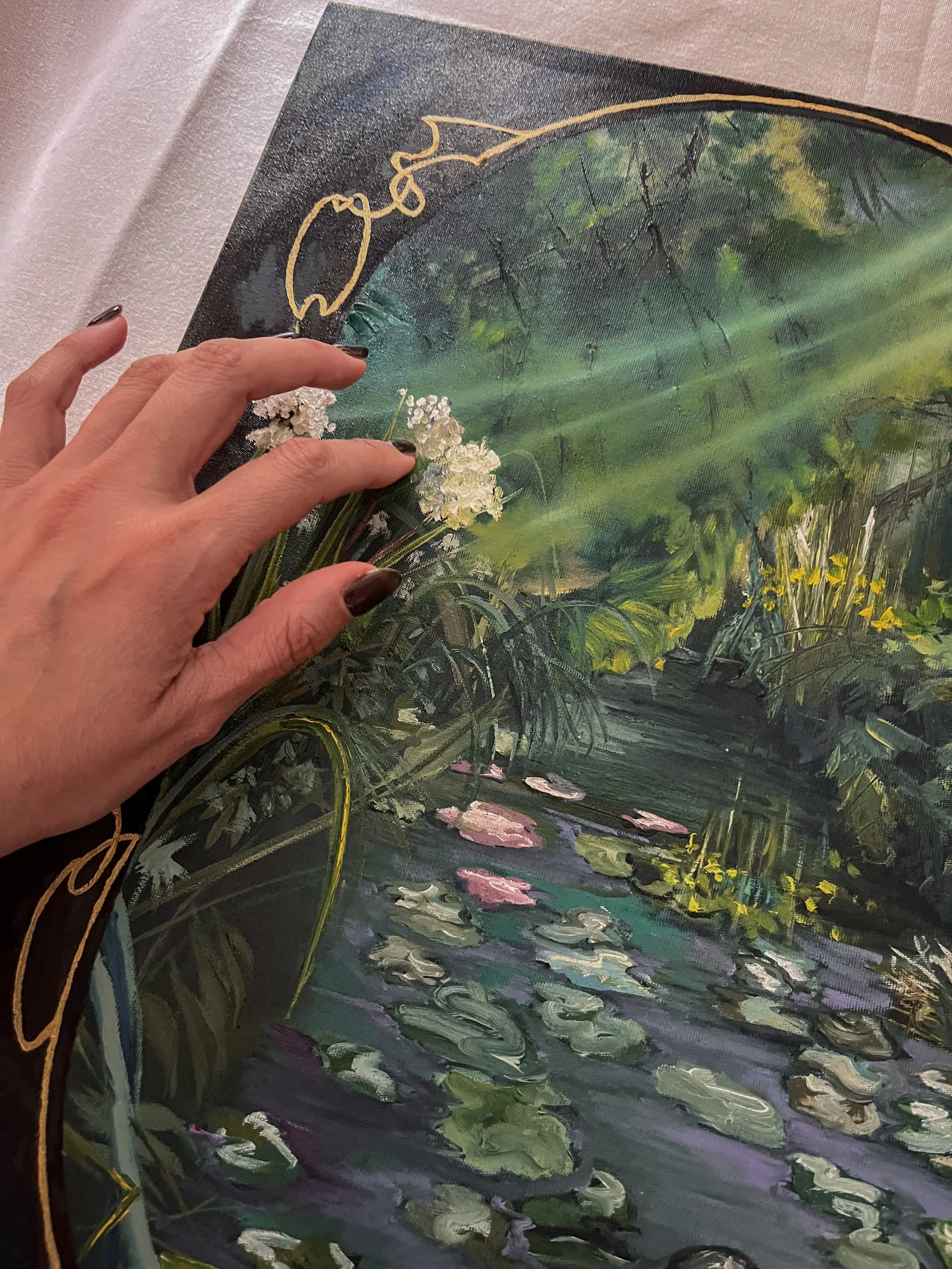 Close-up of a person touching a detailed painting of a serene pond scene with lily pads, flowers, and lush greenery, painted in an impressionist style.