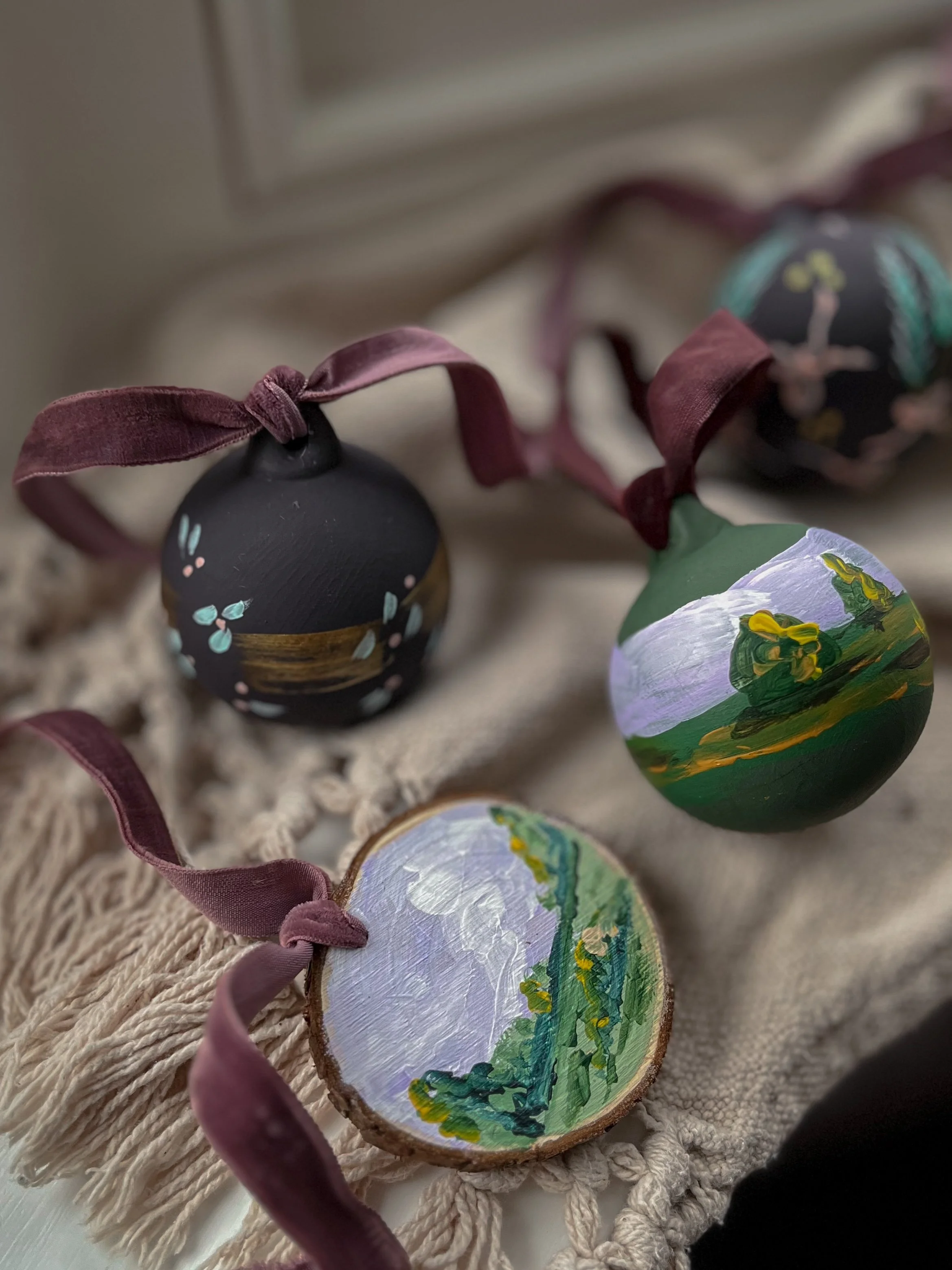 Bespoke hand-painted Christmas baubles with botanical and nature-inspired designs, finished with burgundy ribbon bows.
