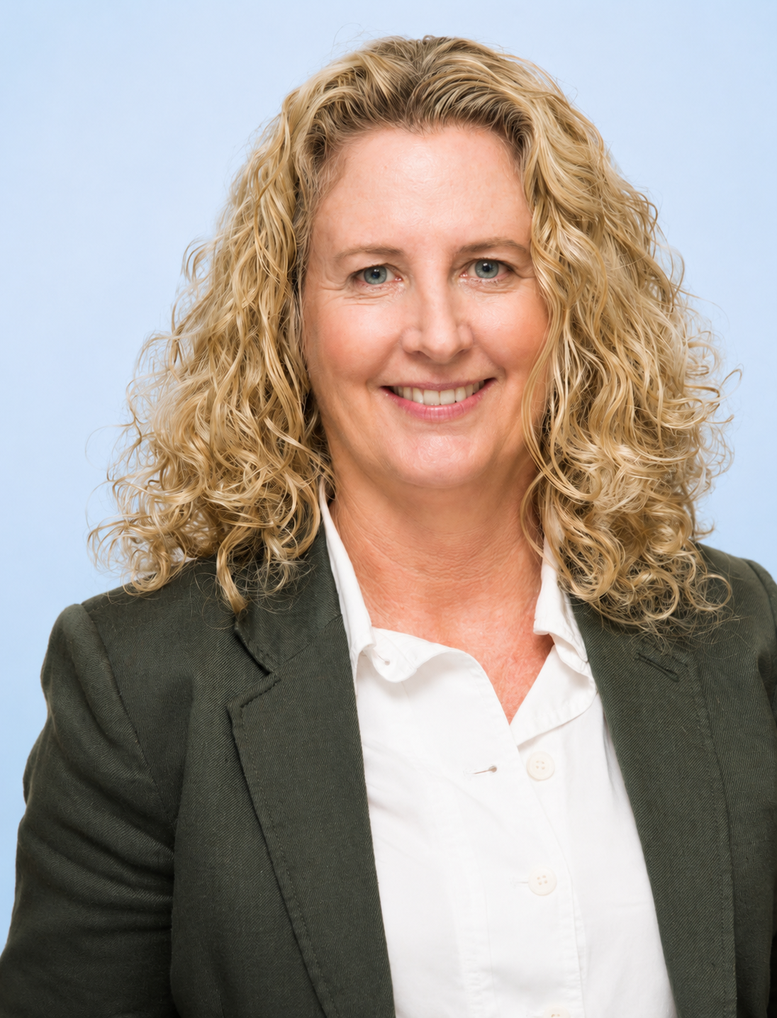 Headshot of a woman with curly blonde hair wearing a dark blazer and white shirt against a light blue background.