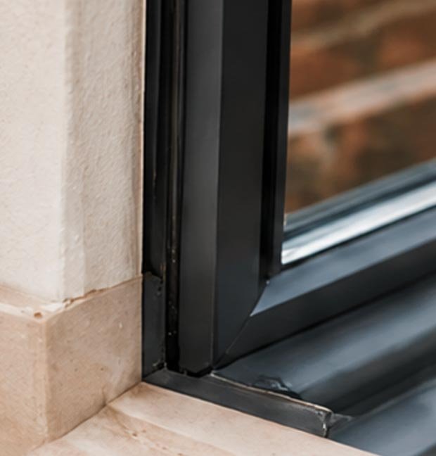 Close-up of a window frame and sill with black metal framing and a stone ledge, showing part of the window and exterior view.
