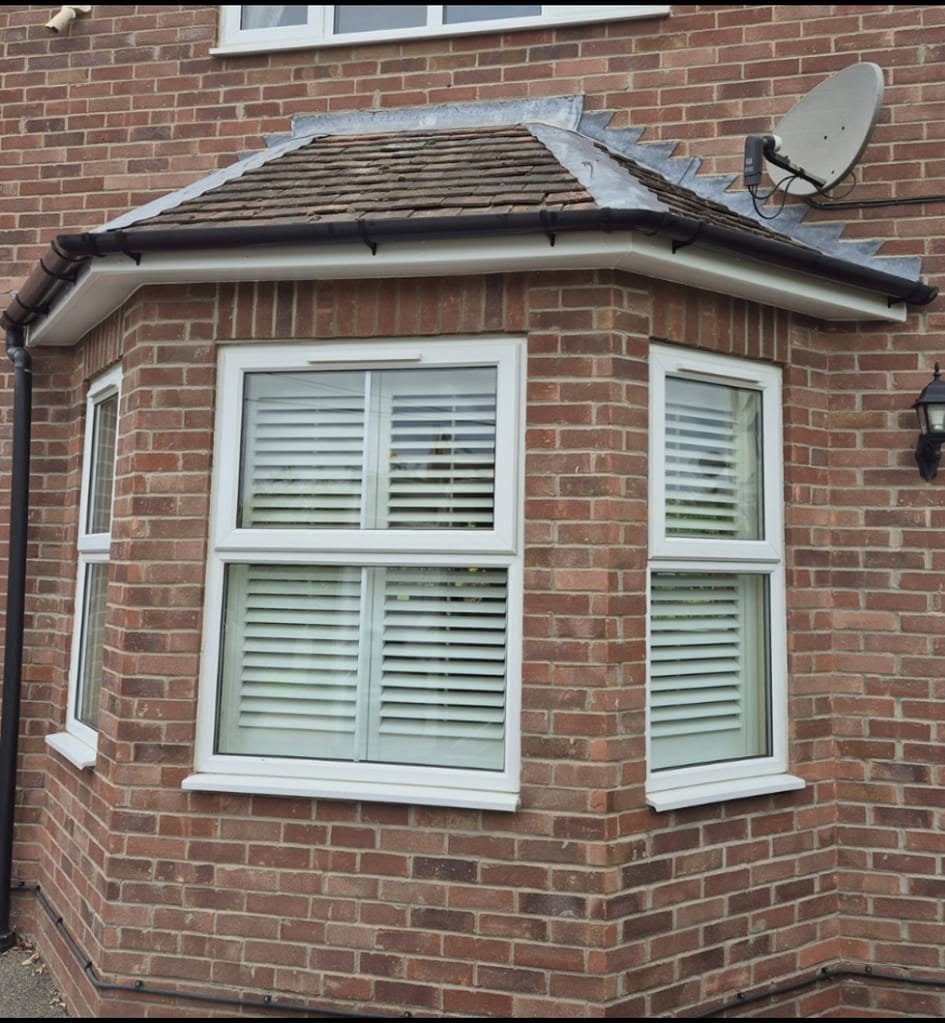 Close-up of the corner of a red brick house with two white double-hung windows with closed blinds and a satellite dish installed on the upper right side.