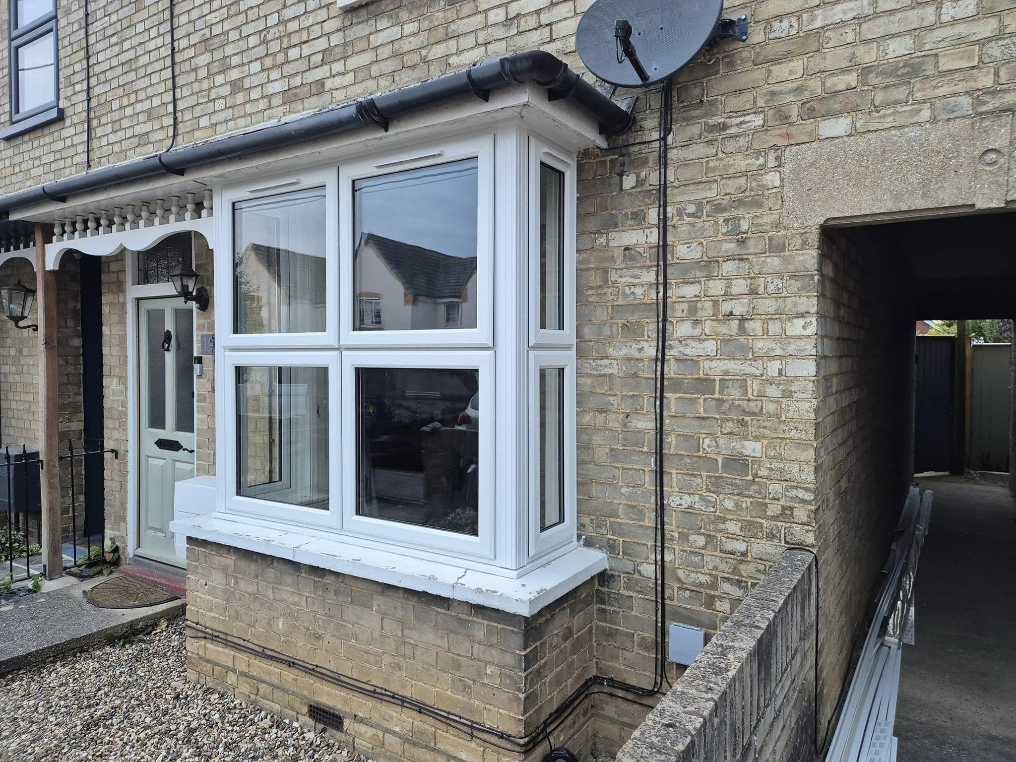 A corner of a brick house exterior with a window, a satellite dish, and black pipework.