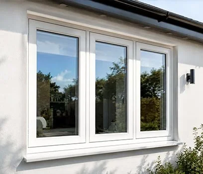 A large white window with three glass panels on a white exterior wall, reflecting trees and blue sky.