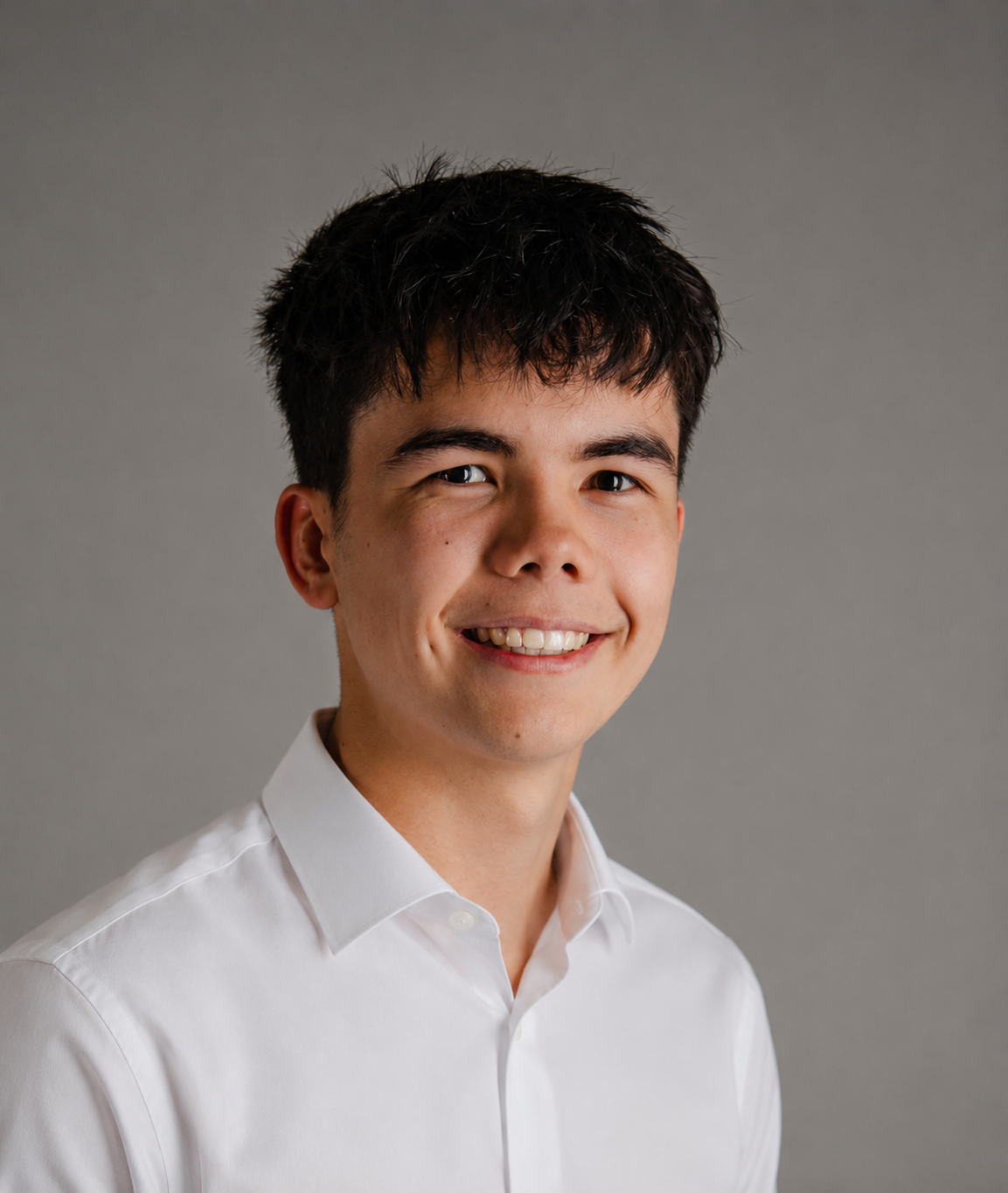 A young man with dark hair and a white button-up shirt smiling against a gray background.