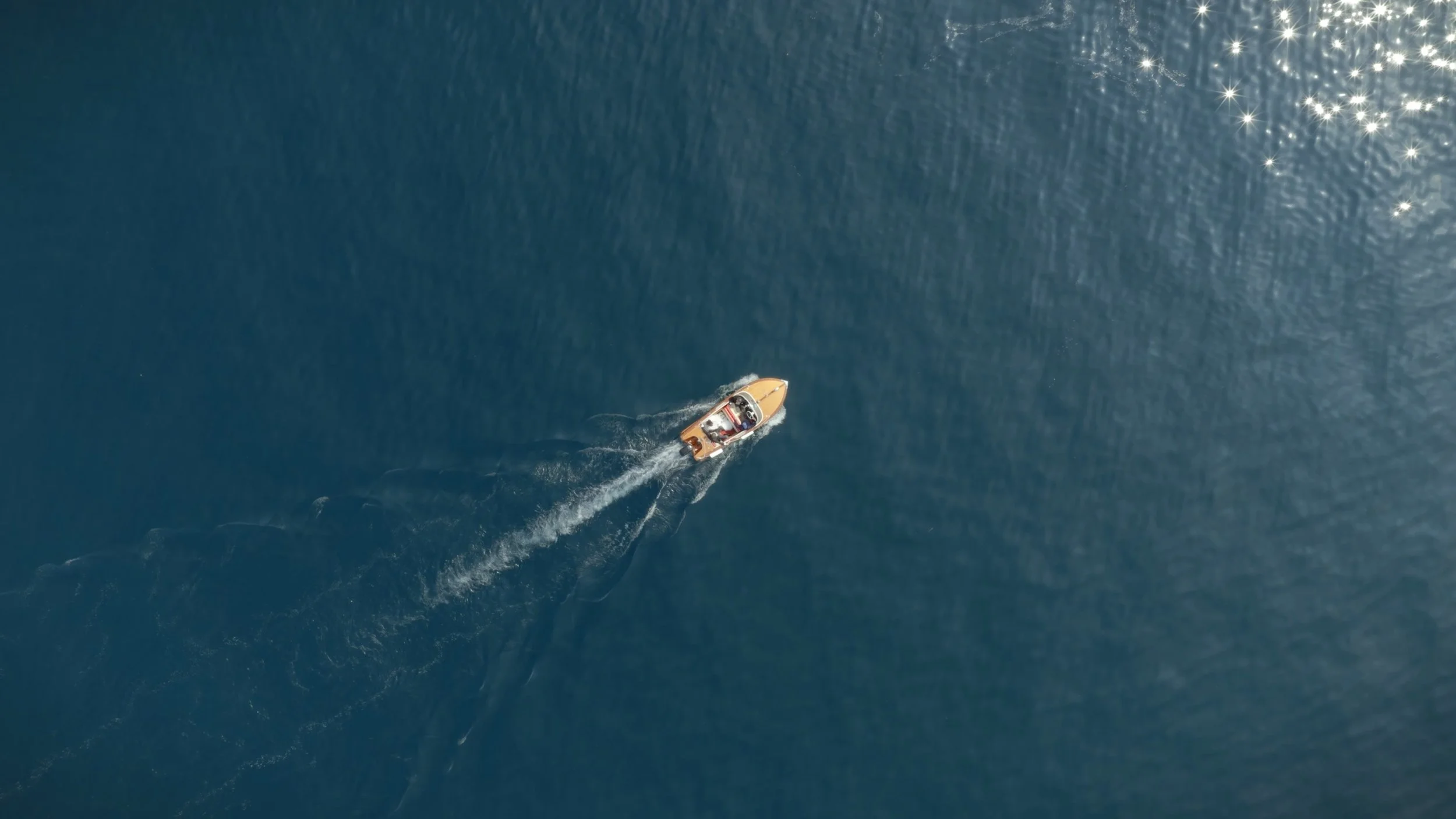 An aerial view of a boat traveling on calm blue water, leaving a wake behind.