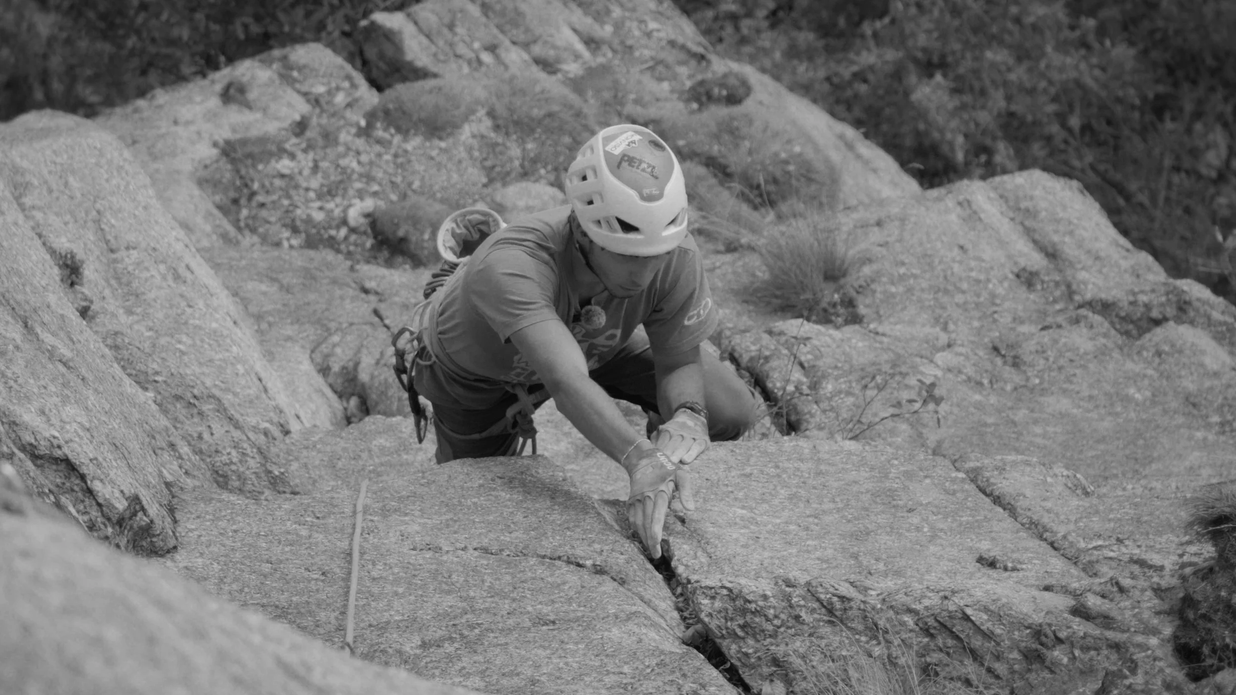 A person wearing a helmet and climbing gear on a steep rock face, mid-climb outdoors.