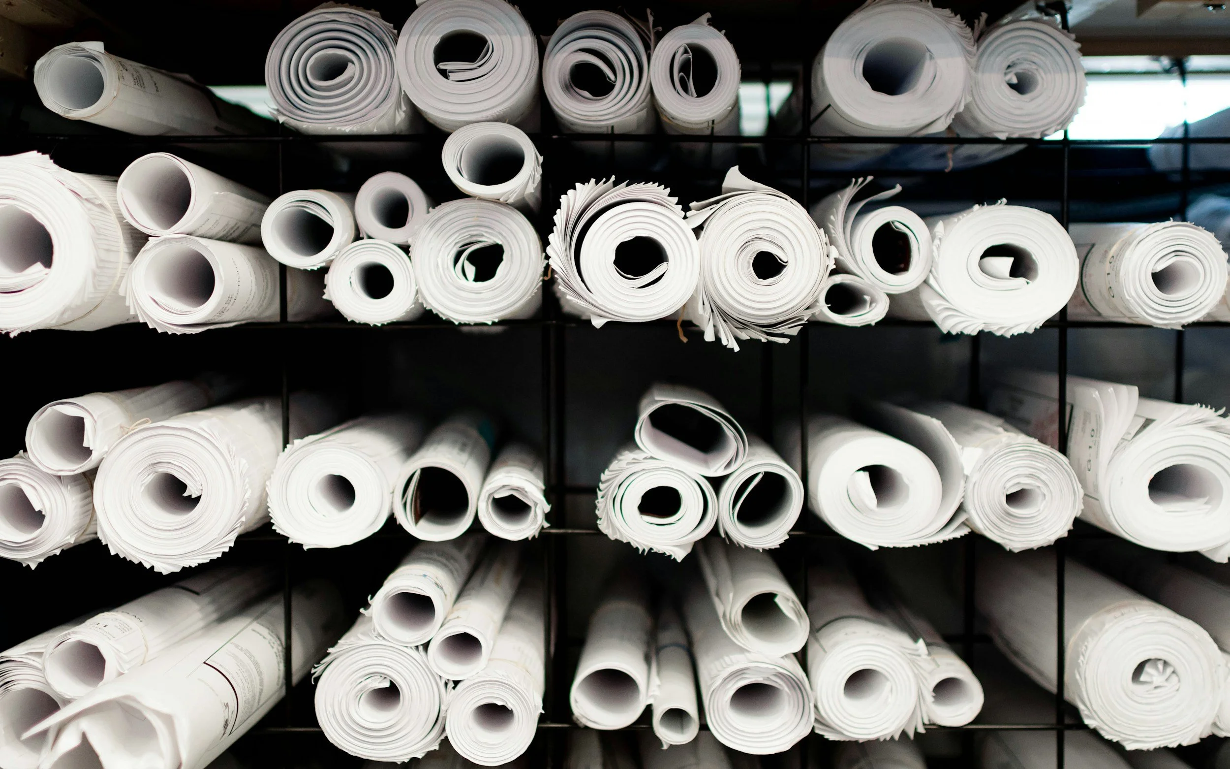Multiple rolled-up architectural or engineering blueprints stored on black shelves.