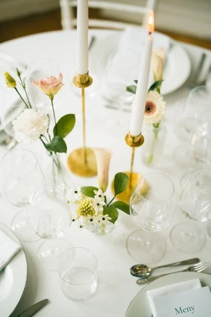 Elegant borddukning med ljuslyktor, blommor och tomma glas, samt ett menykort.