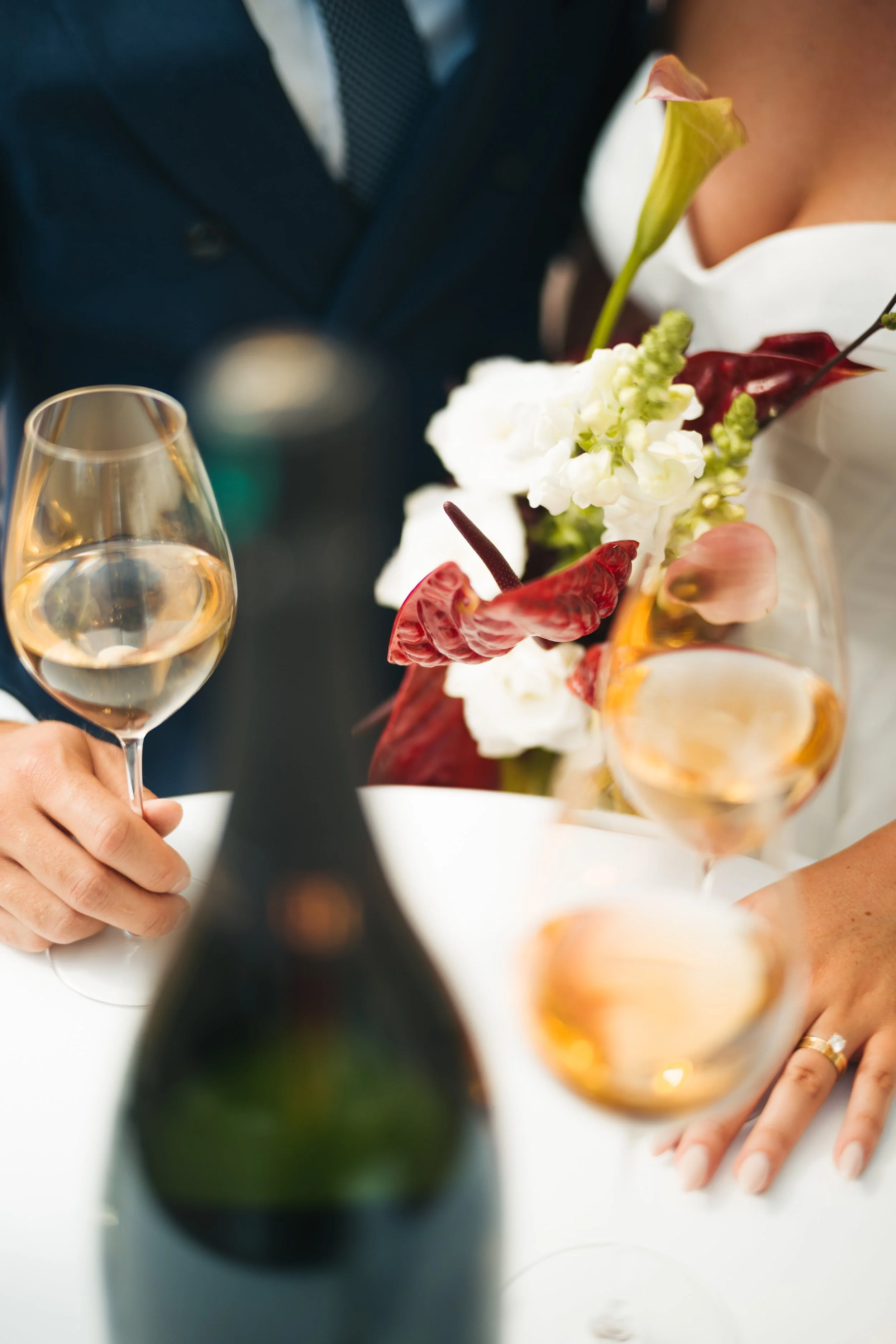 En person som håller ett glas mousserande vin, med ett bröllop eller festtema, inklusive en blomsterbukett med vita och rosa blommor, samt någon som bär en vit klänning.