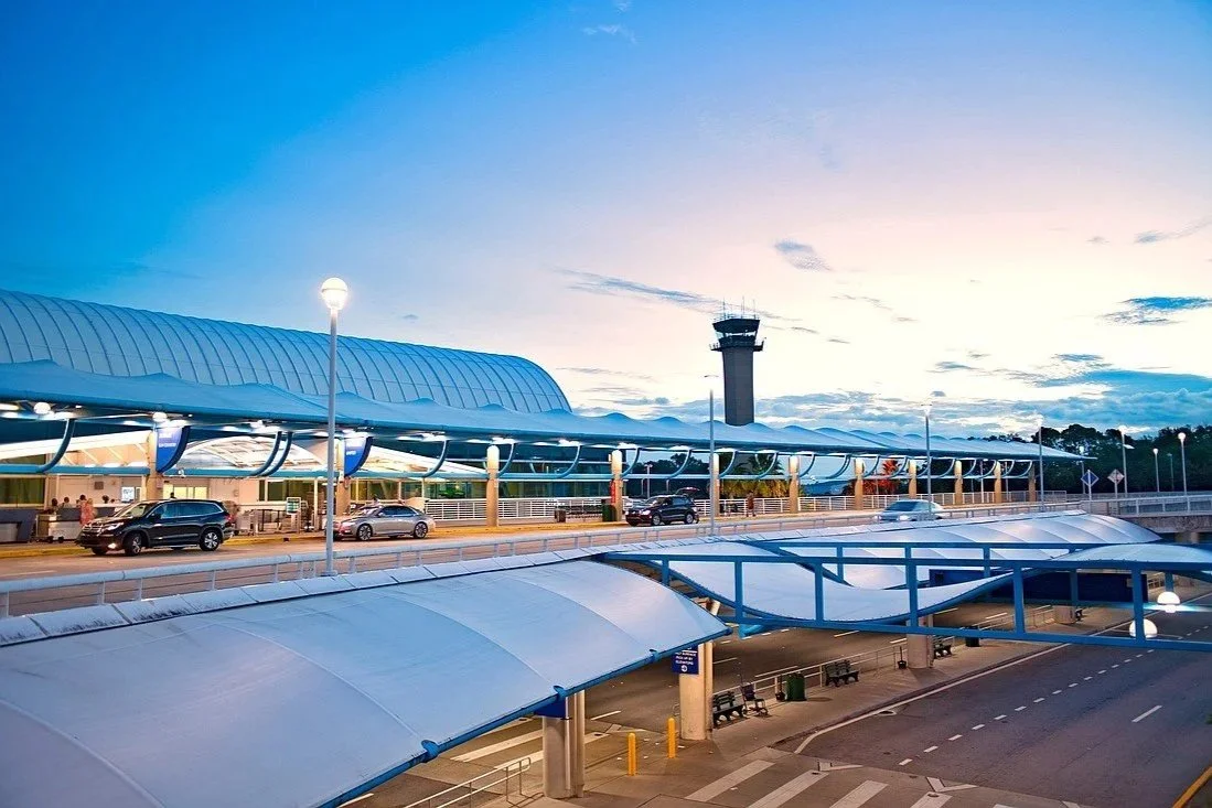 View of Jacksonville International Airport during dusk with cars parked outside, a control tower in the background, and the sky transitioning from day to night.