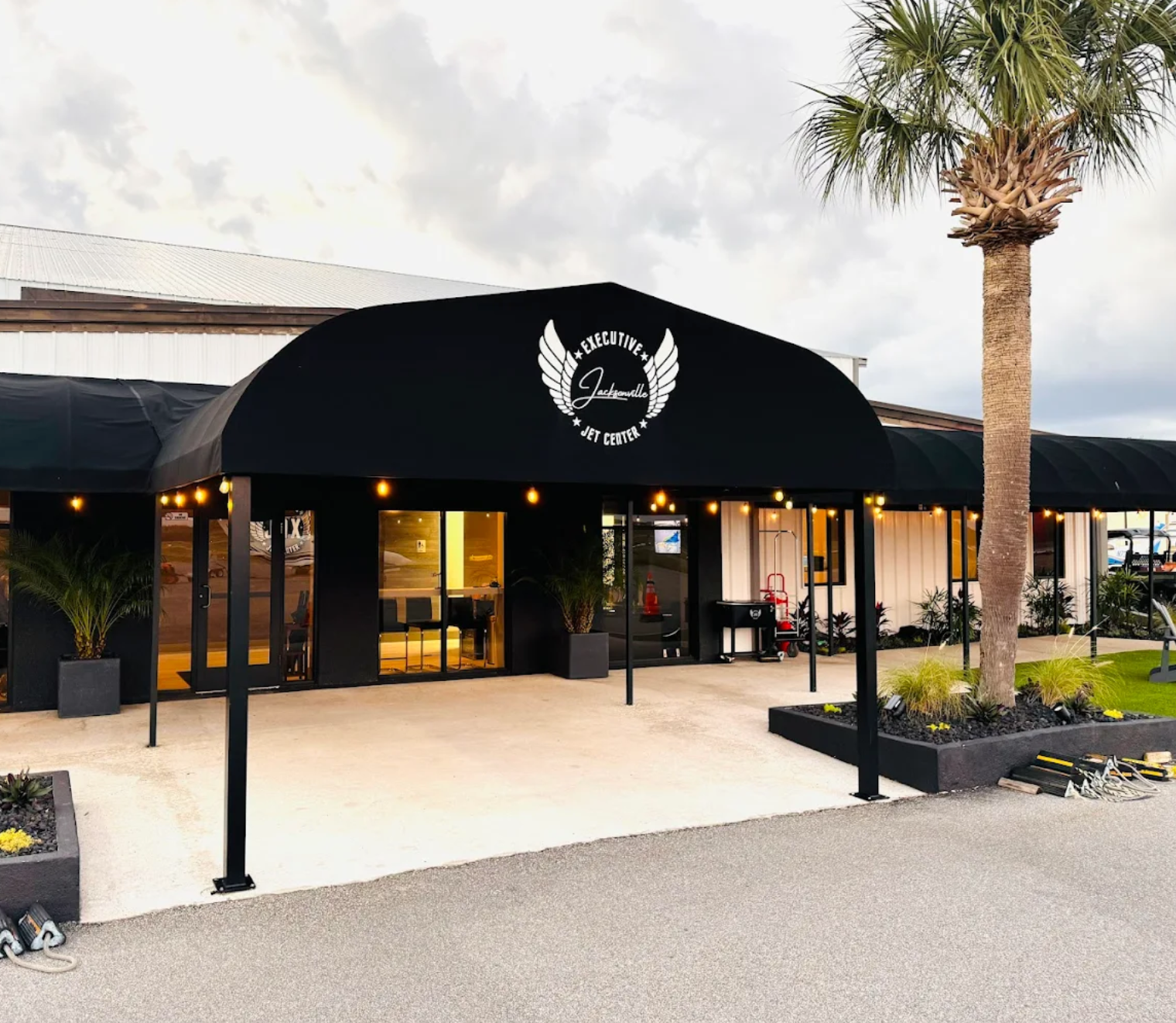 Front entrance of Jacksonville Executive Jet Center', located in Jacksonville, FL, with a winged logo, palm tree, potted plants, and outdoor lighting