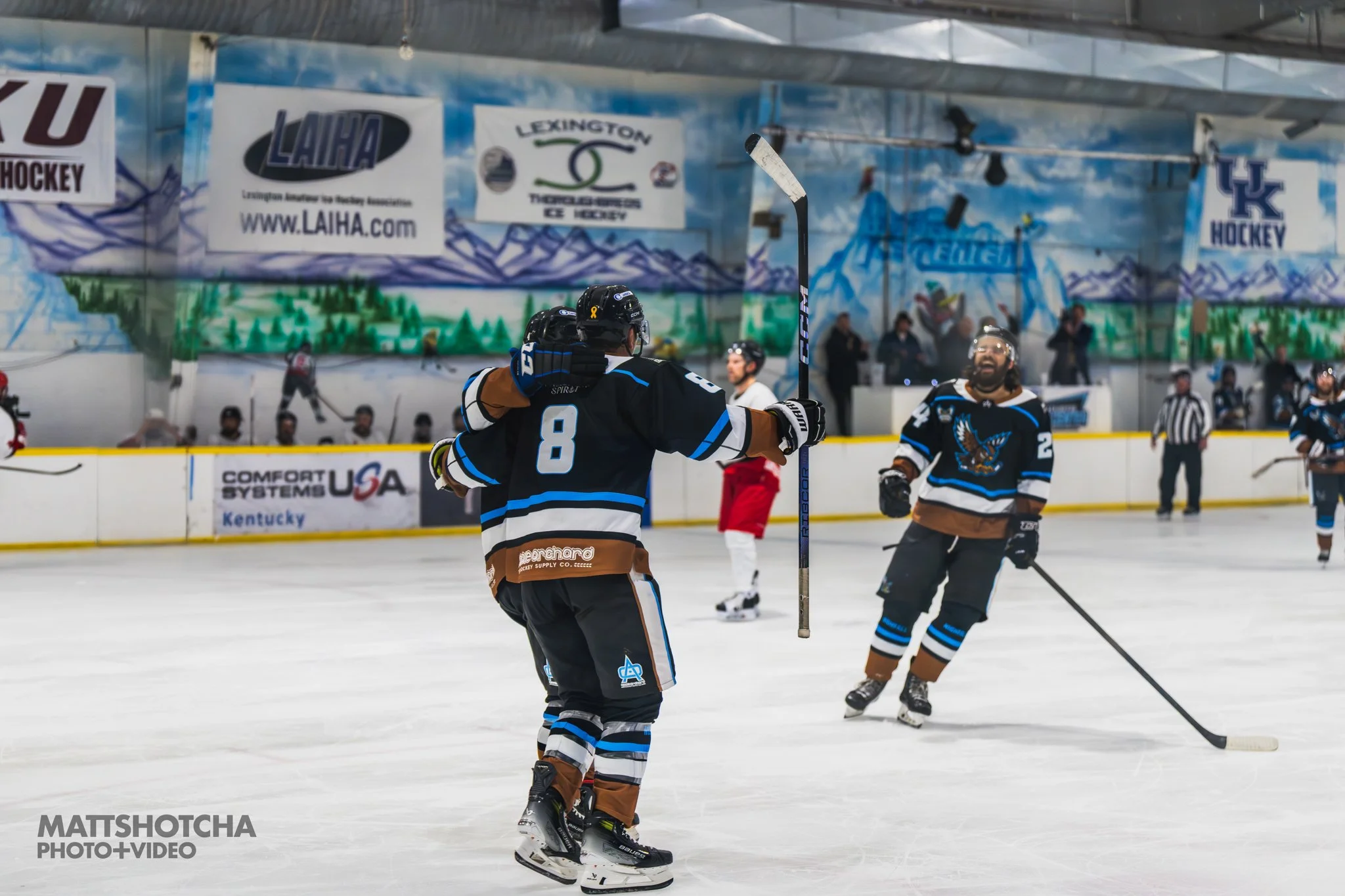 Lexington Nightfall players celebrating on the ice rink, with some players skating and others reacting joyfully, in a hockey arena with banners and spectators in the background.