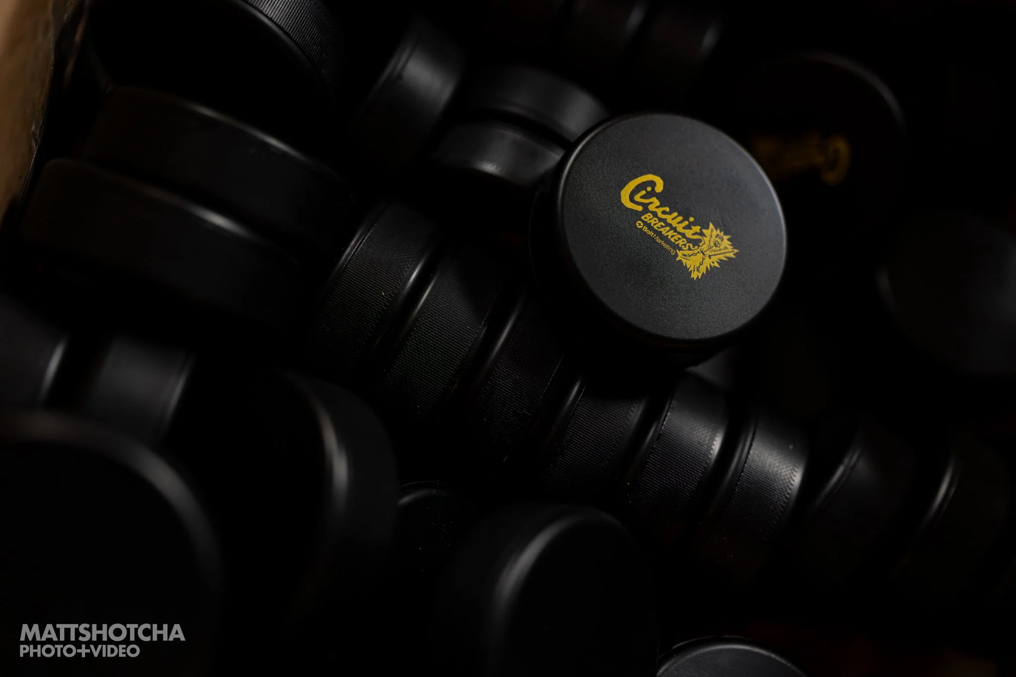 Stack of black hockey pucks with a focus on one with a yellow logo that says 'Circuit Breakers' and features a logo.