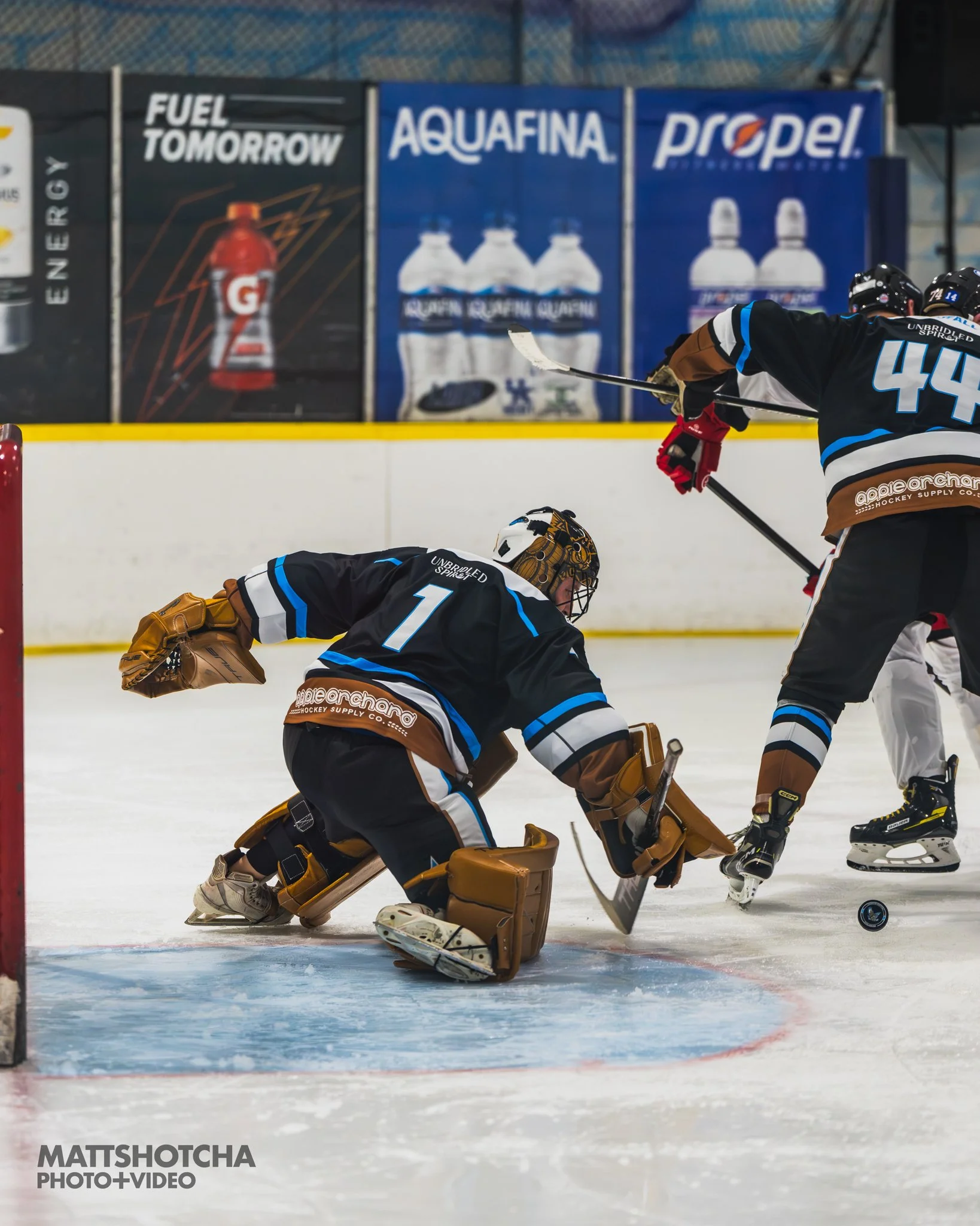 Lexington Nightfall goalie in black and teal gear making a save during a game, with other players nearby and advertisements in the background.