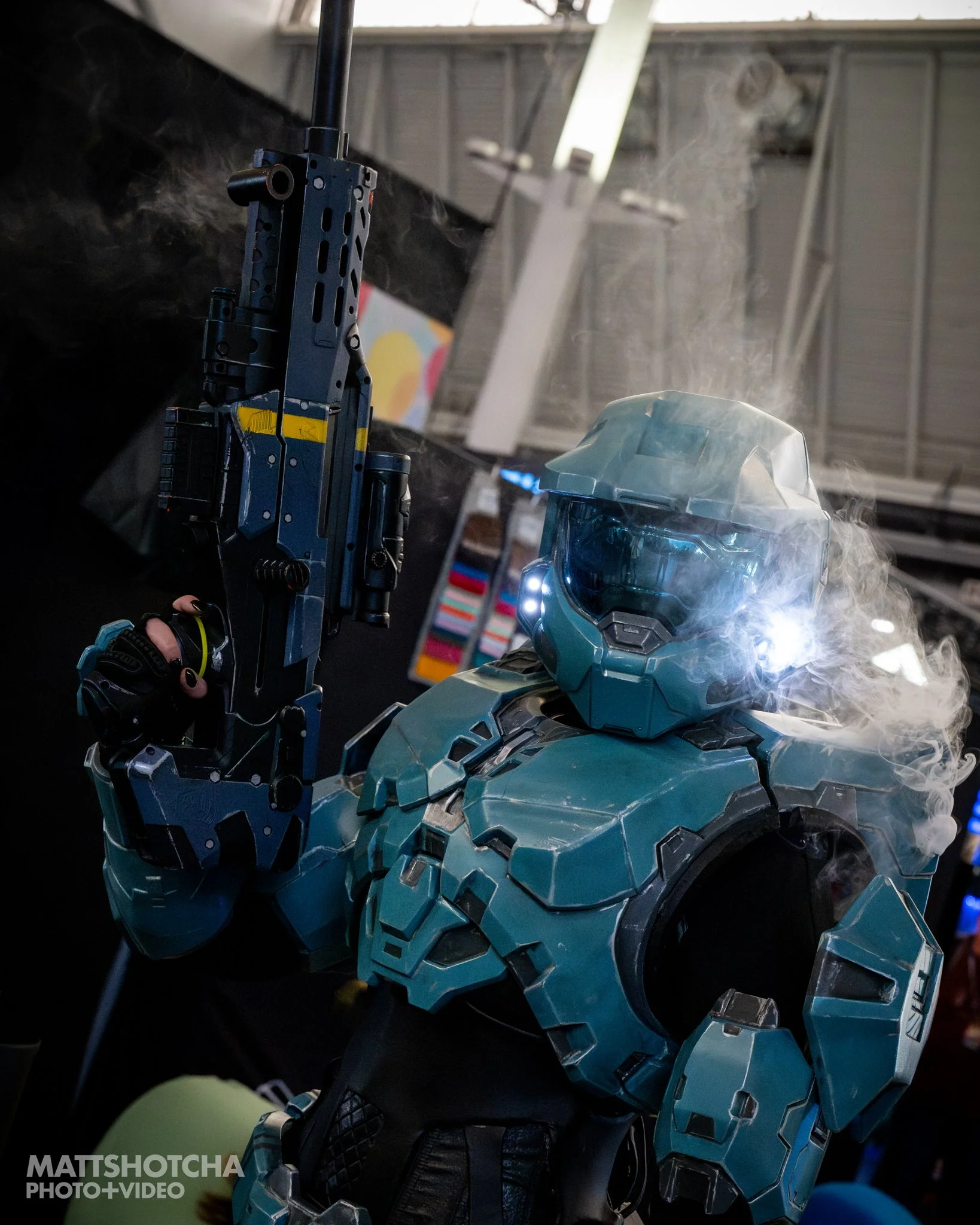 Up-close view of a man dressed as Master Chief from Halo, with a futuristic design, surrounded by smoke, with a large head and illuminated eyes, posed in the convention center at PAX East 2026.