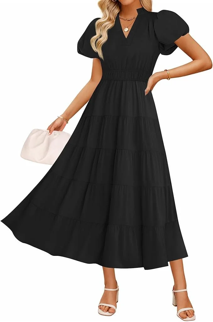 Woman wearing a black, tiered maxi dress with puffed short sleeves, paired with white heels, holding a white purse, and accessorized with necklaces and bracelets.