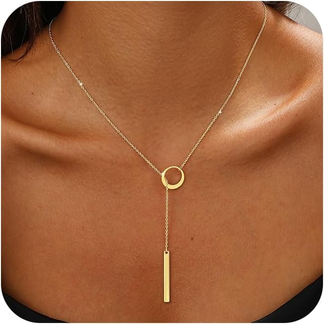 Gold necklace with a circular pendant and a vertical bar hanging from it, worn on a person's neck.