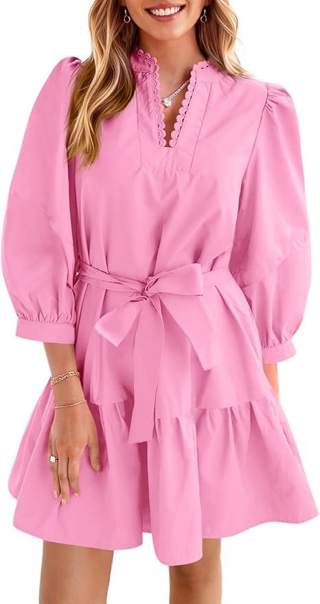 A woman wearing a pink dress with puff sleeves, lace collar, a belt tied in a bow, and a ruffled hem, accessorized with jewelry.