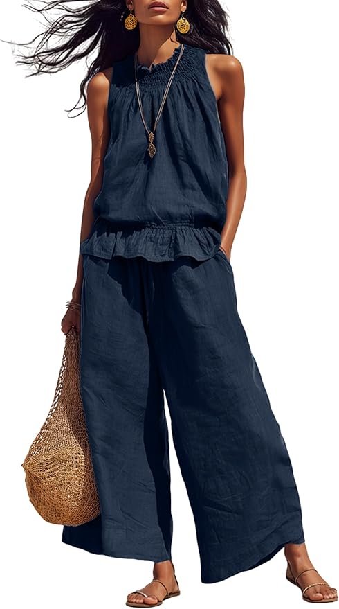 Woman wearing a dark blue sleeveless top and wide-leg pants, accessorized with gold earrings and a long necklace, holding a large woven straw bag.