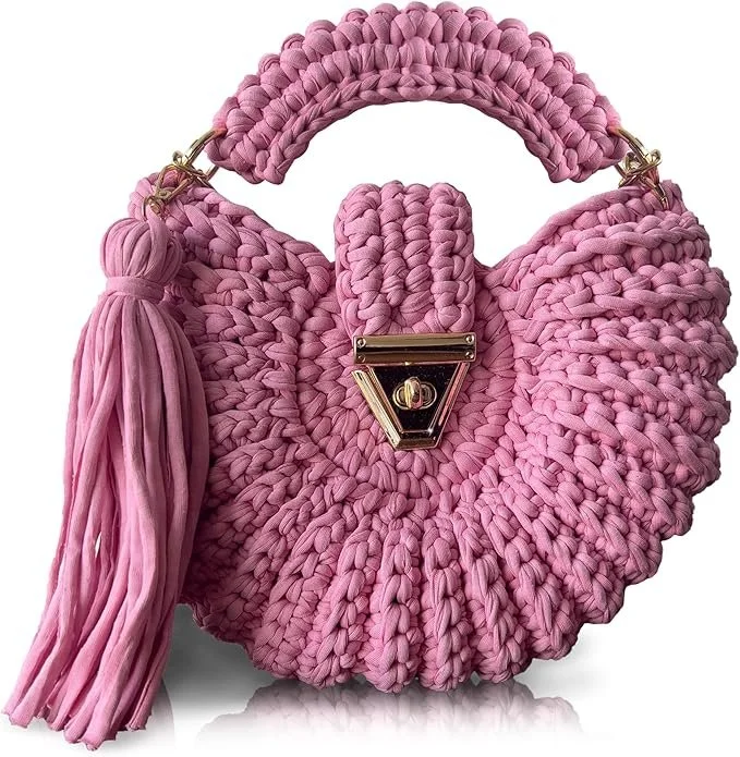 Pink chunky knit handbag with a gold clasp closure and a large tassel on the side, featuring a rounded shape and woven texture.