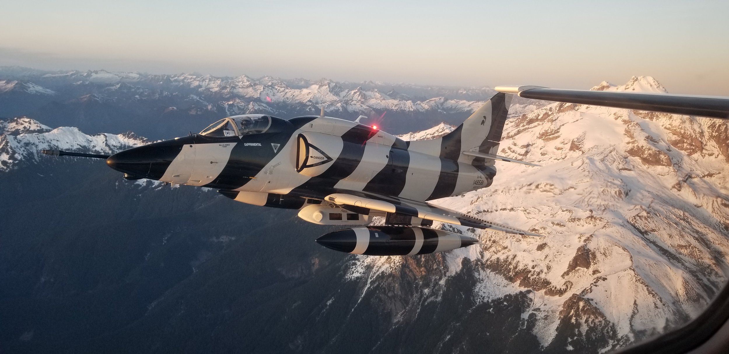 An aircraft flying over snow-capped mountains during sunset or sunrise.