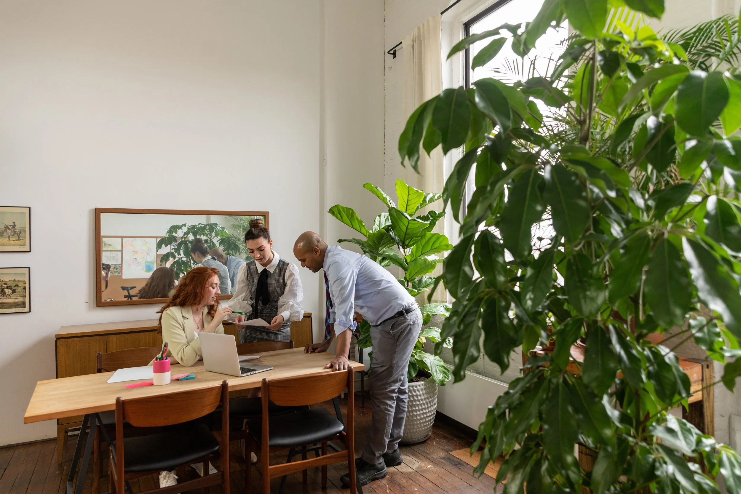 Three professionals reviewing documents together in a bright, plant-filled office space, representing the supportive and collaborative approach of Austen LaBarge LCSW's virtual therapy practice in New York