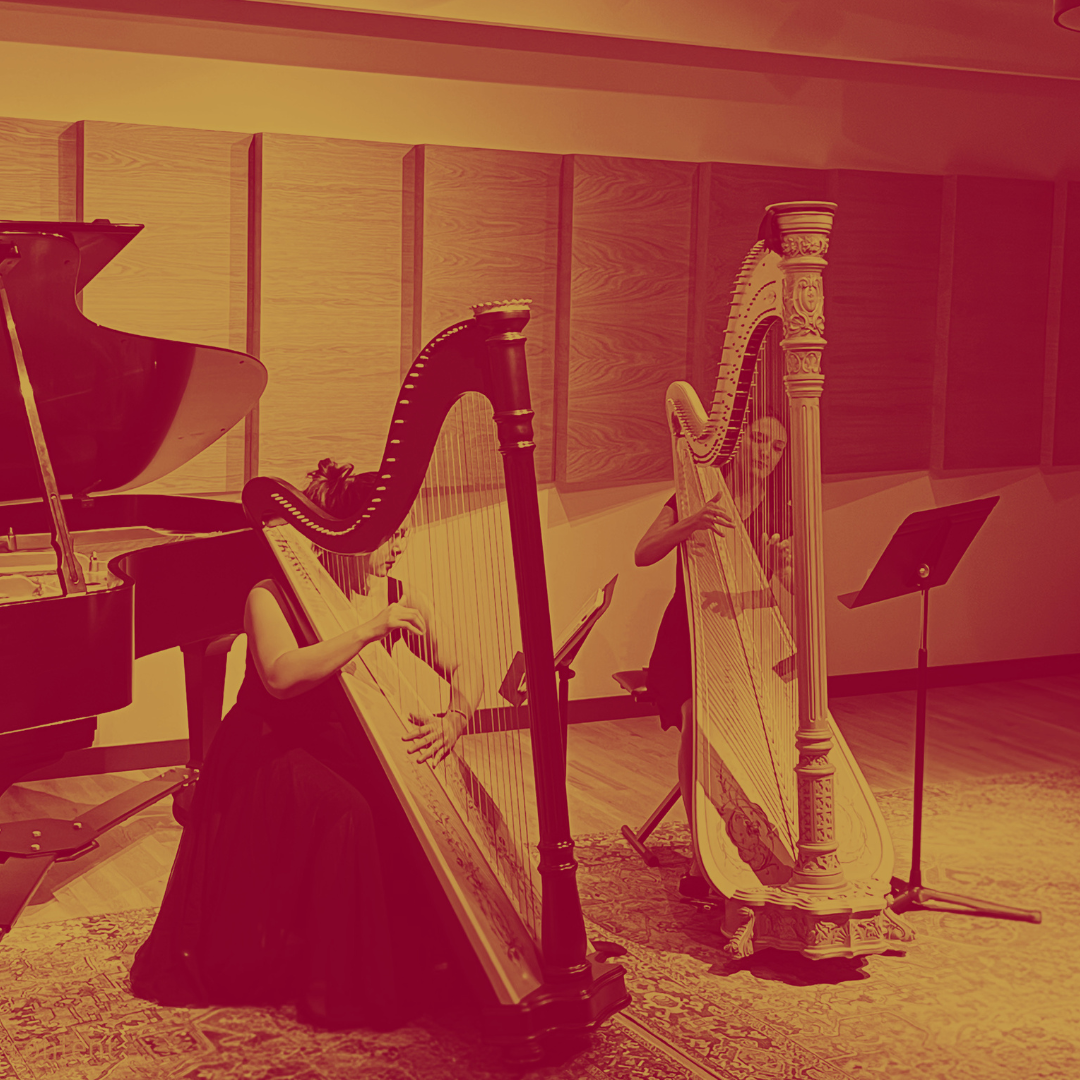 Two women playing harps in a music room with a grand piano and music stands.