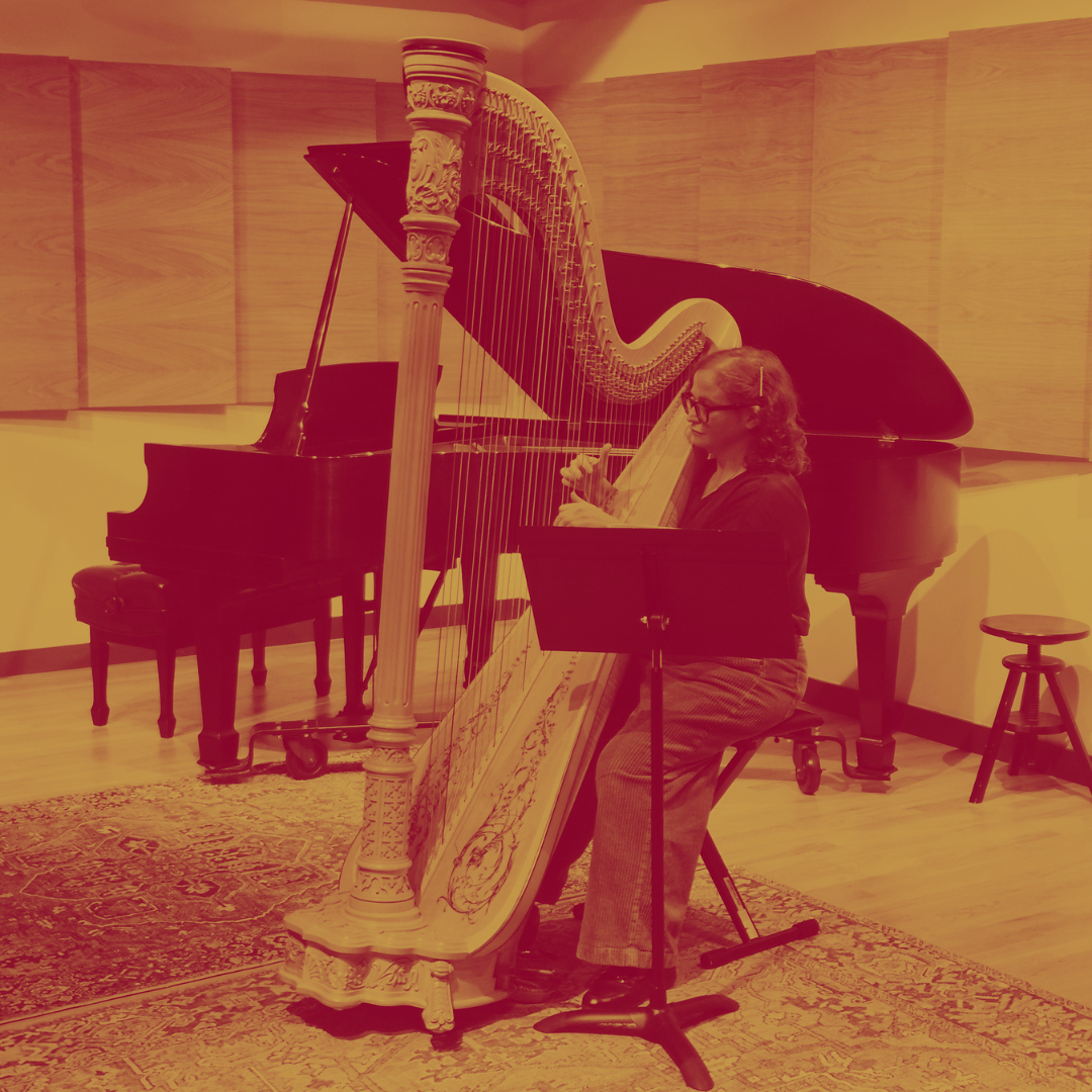 A woman playing a harp and a grand piano in a music studio.