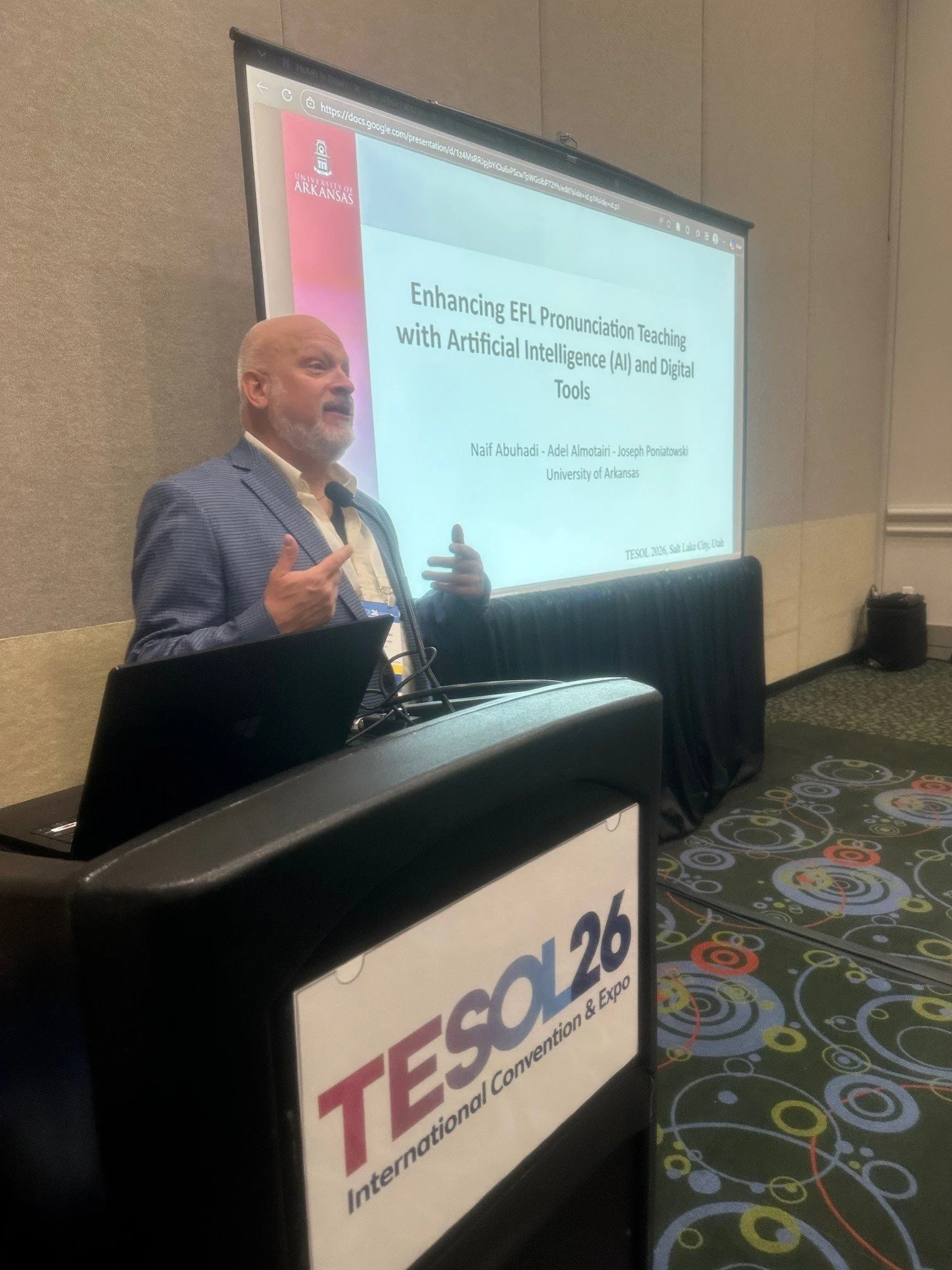Joseph standing in front of a large screen displaying a PowerPoint slide with the title ‘Enhancing EFL Pronunciation Teaching with Artificial Intelligence (AI) and Digital Tools,’ at the TESOL International Convention & Expo, in Salt Lake City, Utah.