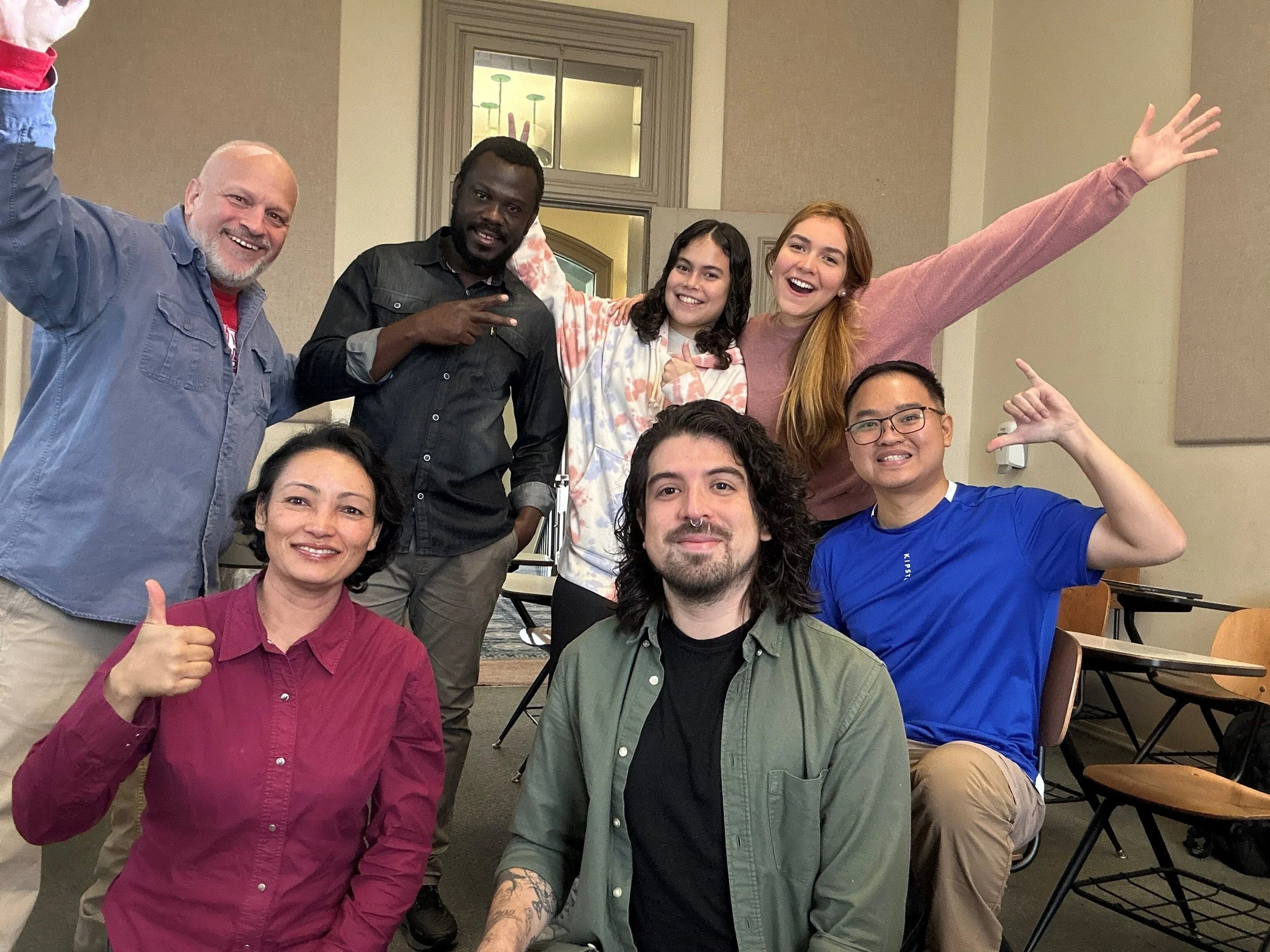A group of international students and Joseph Poniatowski are posing together indoors, some smiling, making gestures, and enjoying each other's company in a classroom at the University of Arkansas.