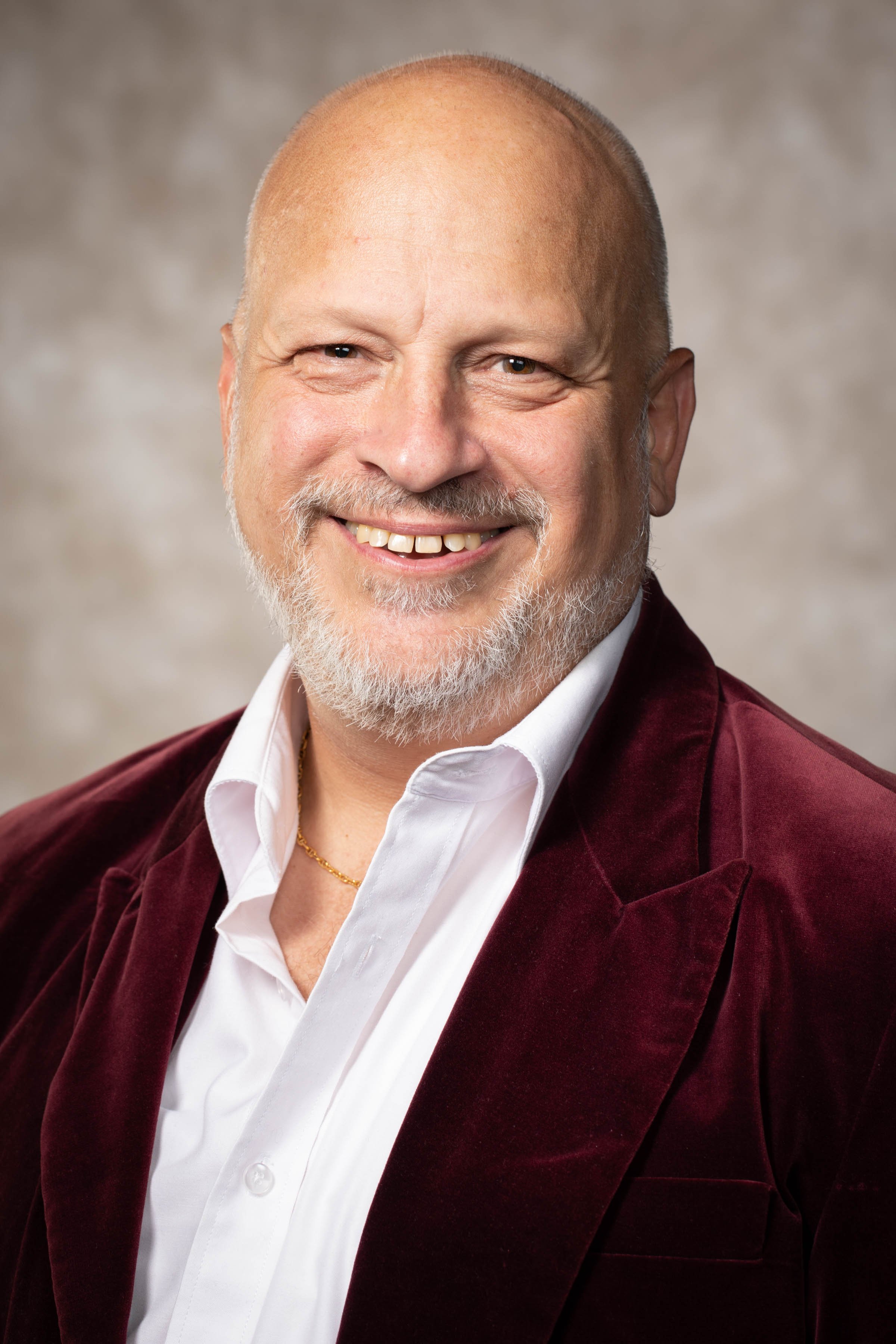 Photo of Joseph Poniatowski wearing a maroon blazer with a white shirt smiling for a professional photograph